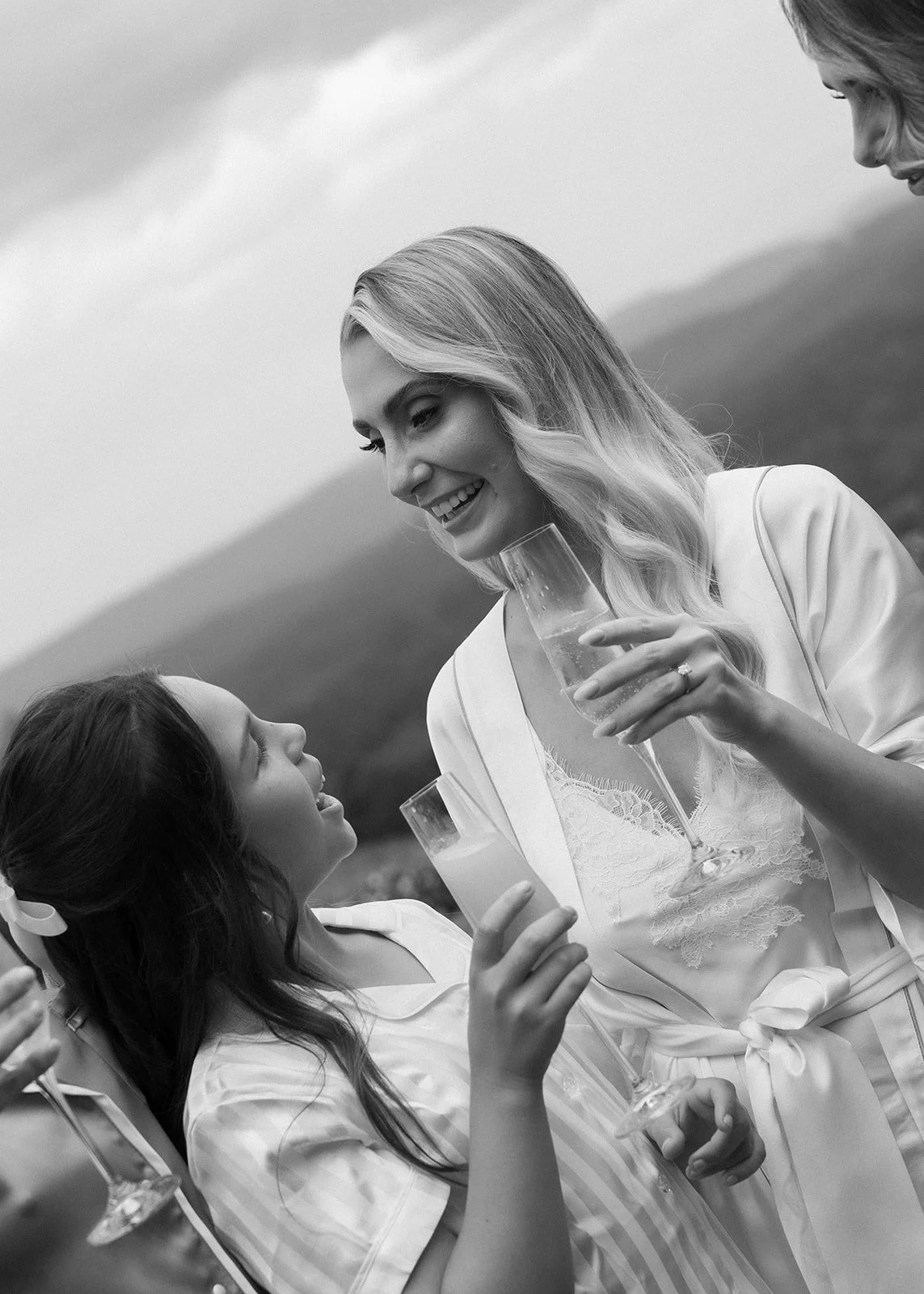 A black and white photo of a woman and a young girl at an outdoor gathering, smiling and holding glasses of champagne. The woman is looking at the girl, and they appear to be enjoying each other's company.
