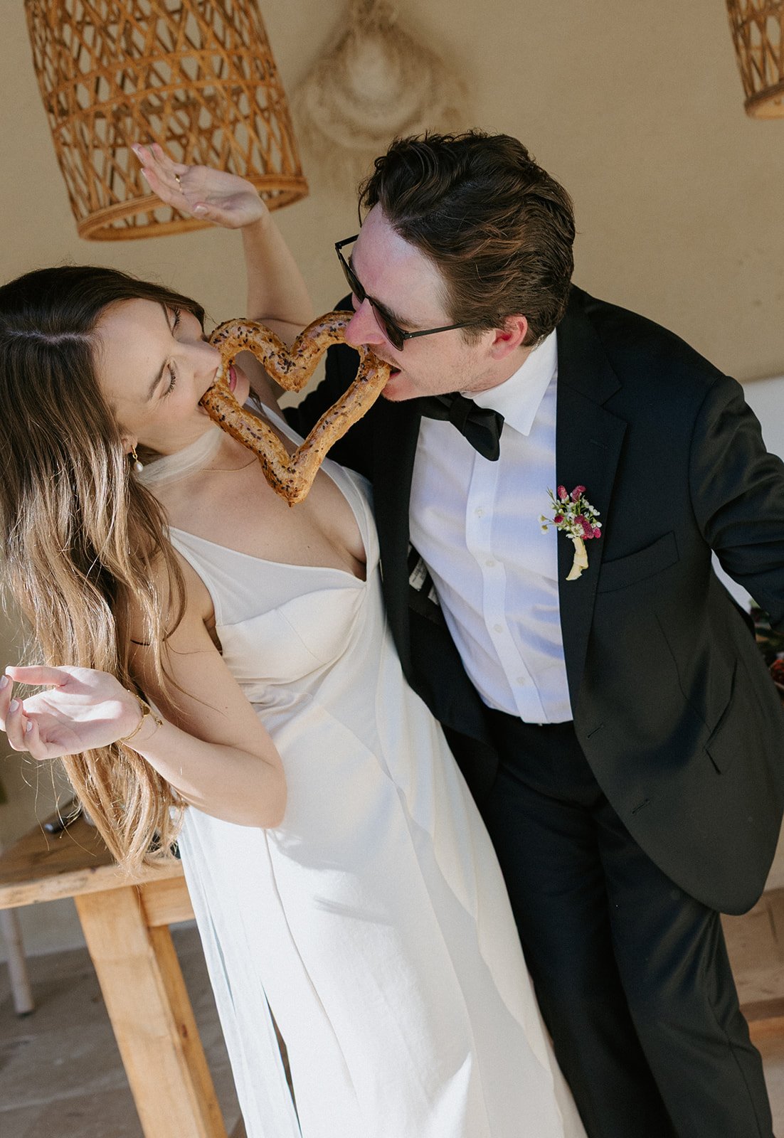 A bride and groom are sharing a playful moment with a heart-shaped pretzel during their wedding celebration.