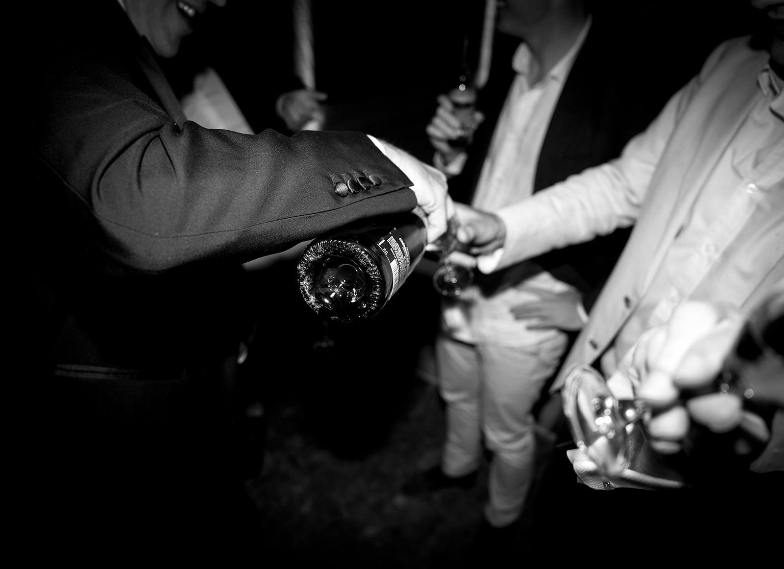 Close-up of a man in a suit pouring champagne into a glass held by another man in a white shirt and blazer at a social gathering.