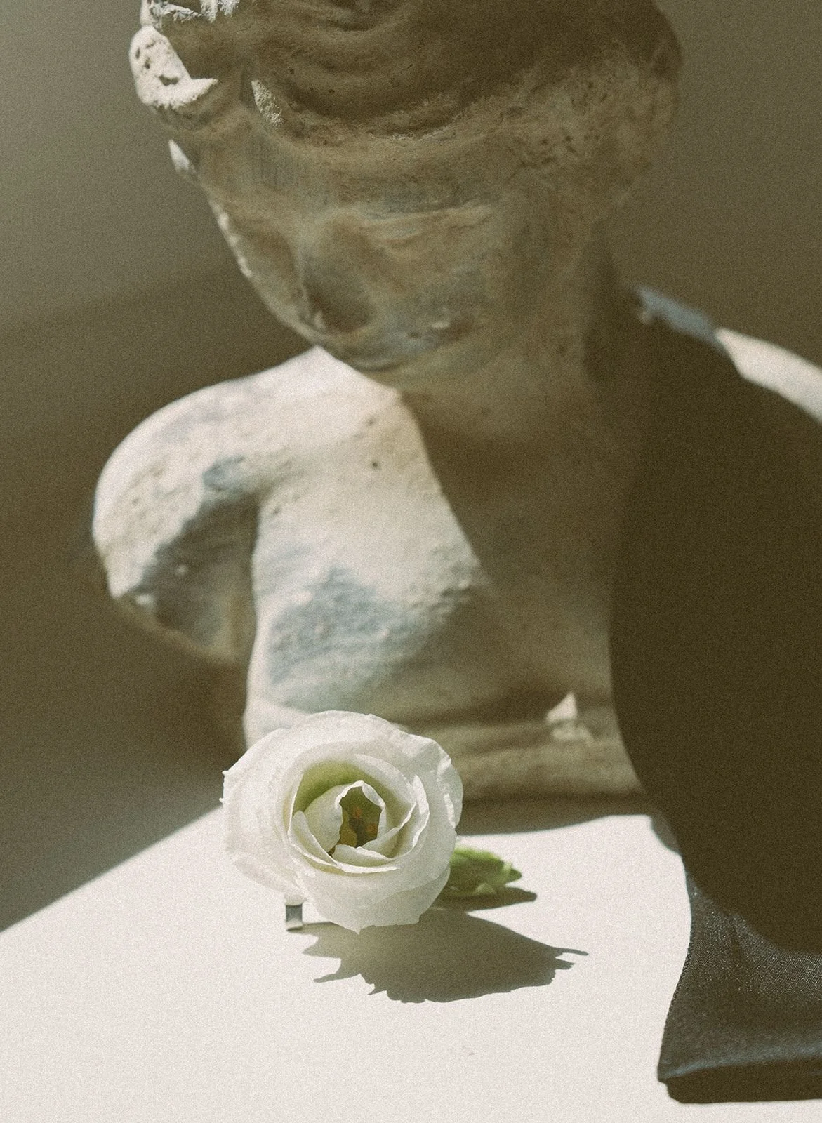 Close-up of a weathered statue of a child with a white flower lying in front of it, casting a shadow.