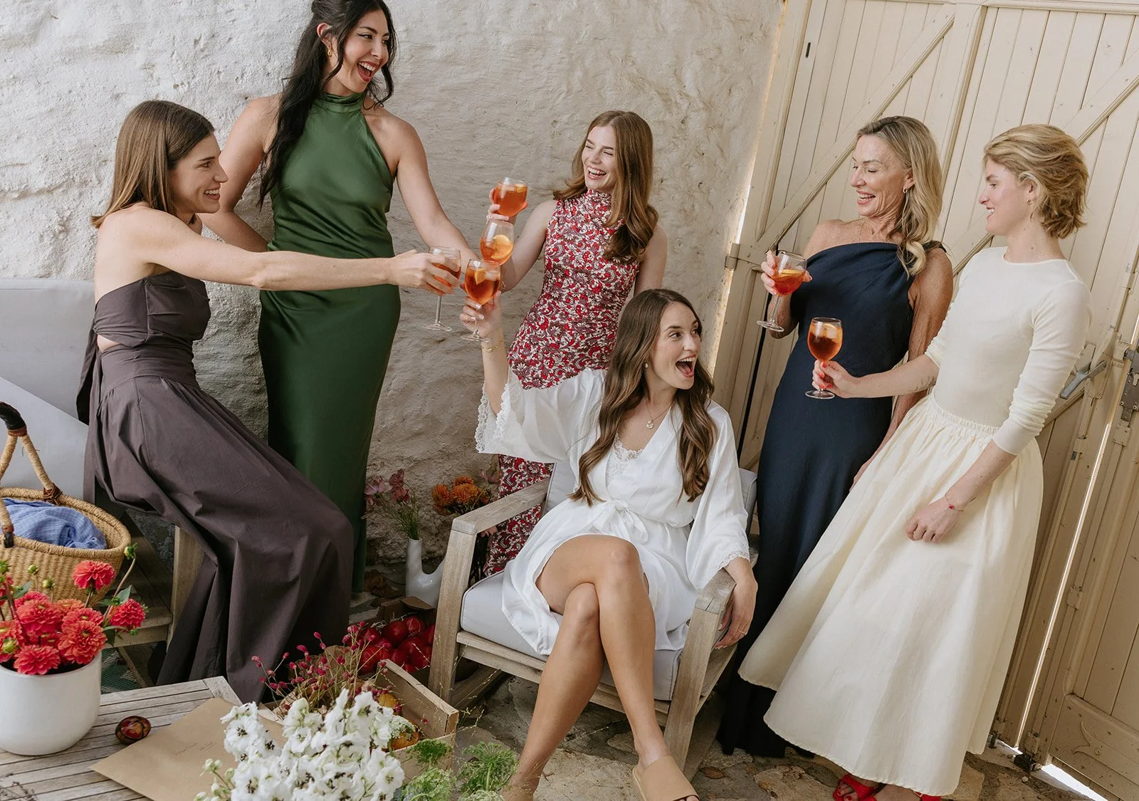 Group of women celebrating with drinks in a cozy, rustic indoor setting, smiling and toasting.
