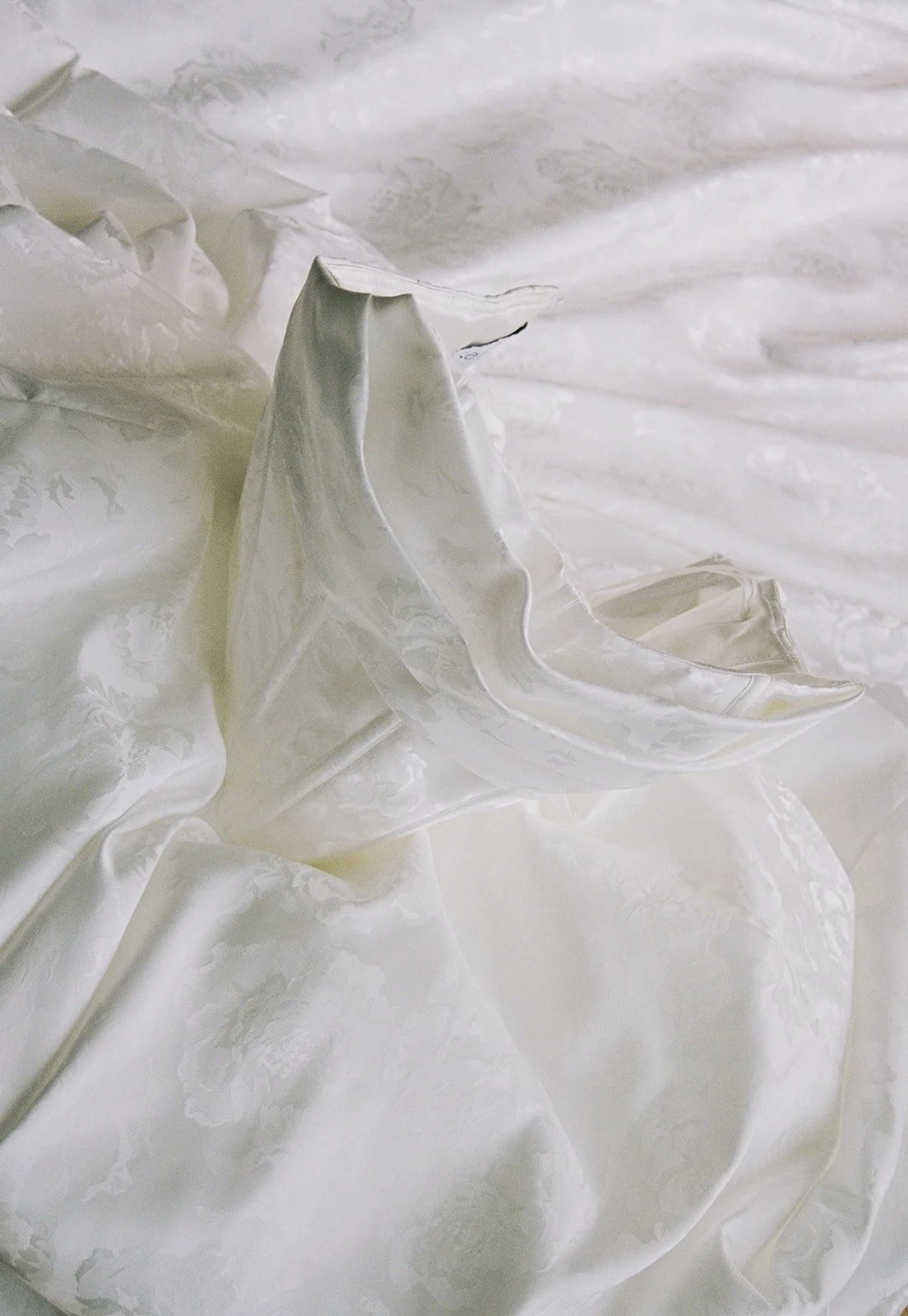 Close-up of white satin fabric with floral damask pattern and ruffled edges.