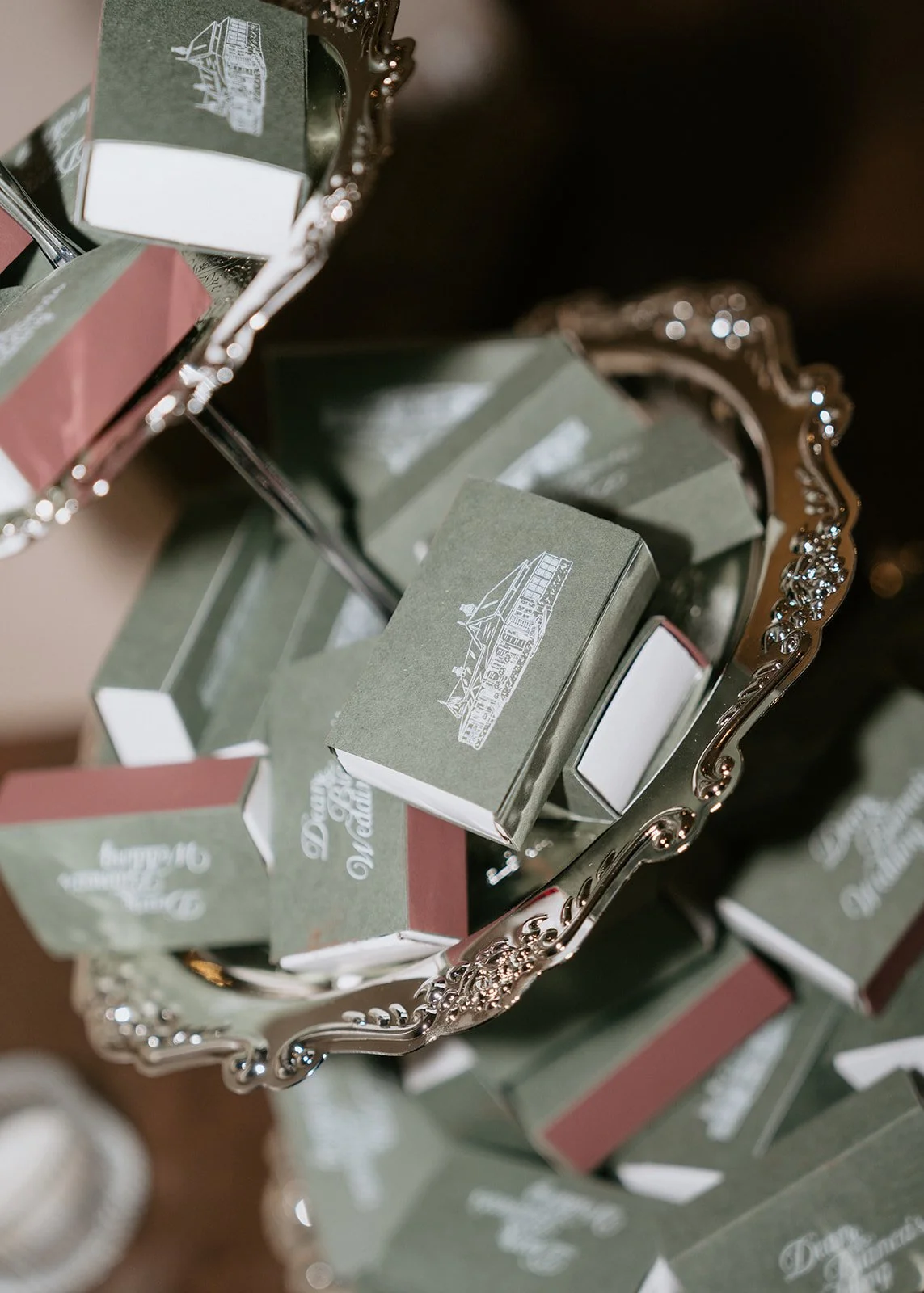 Decorative silver tray filled with small boxed gifts, each wrapped in green paper with white text and illustrations, with other boxes visible in the background.