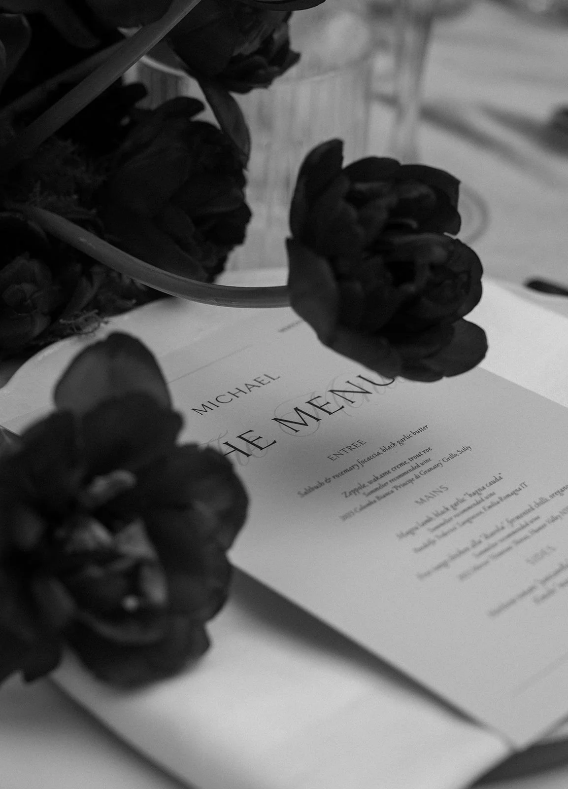 Black and white photo of a printed menu with the title 'Michael' and some floral decorations placed on top.