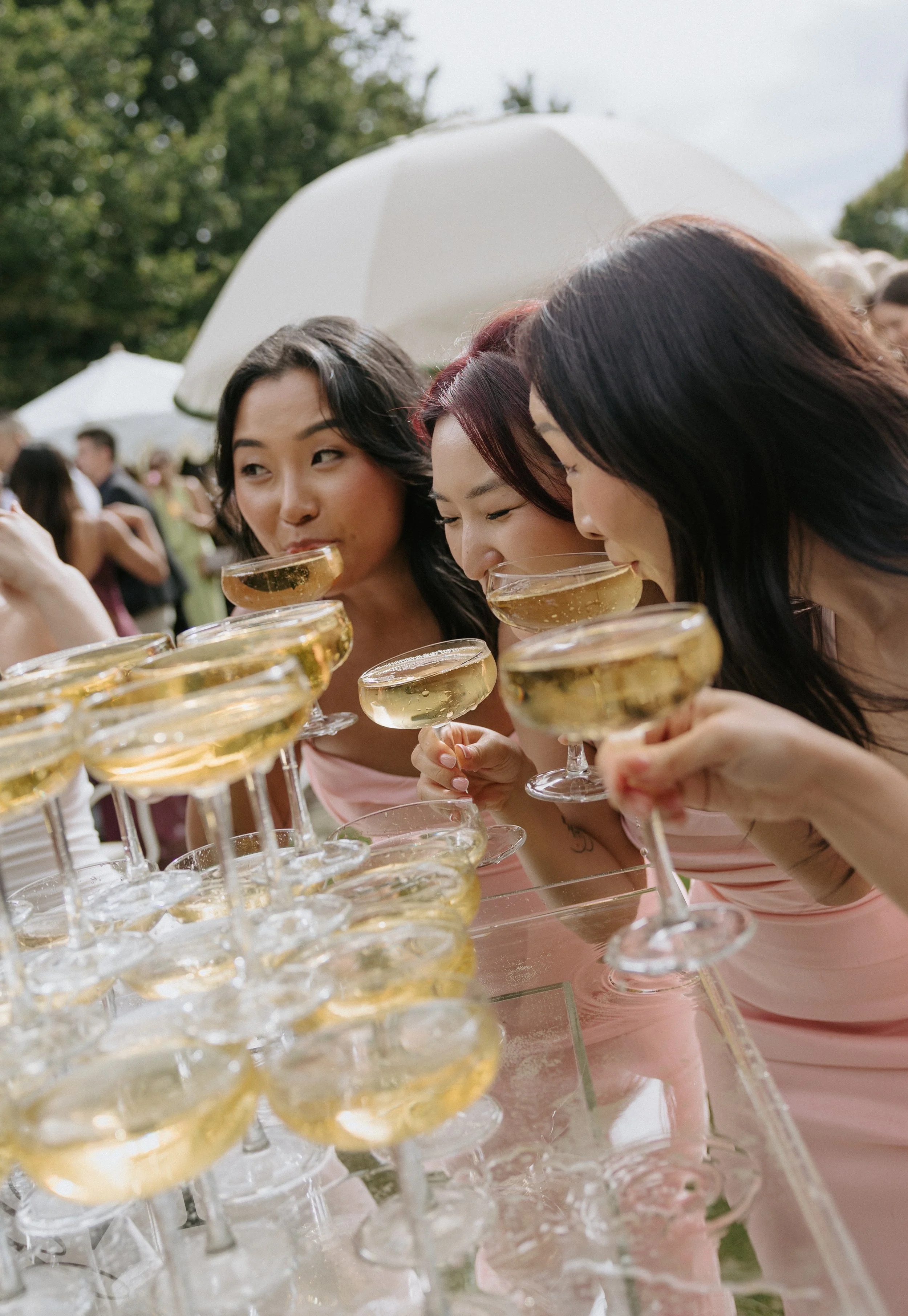 Wedding photography by Brontë McVeigh: Group of women in pink dresses drinking champagne at an outdoor event.