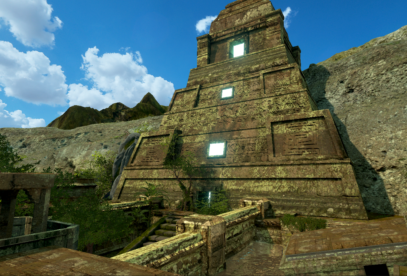 Ancient stepped pyramid with carved hieroglyphics, set against a mountainside and blue sky with clouds.