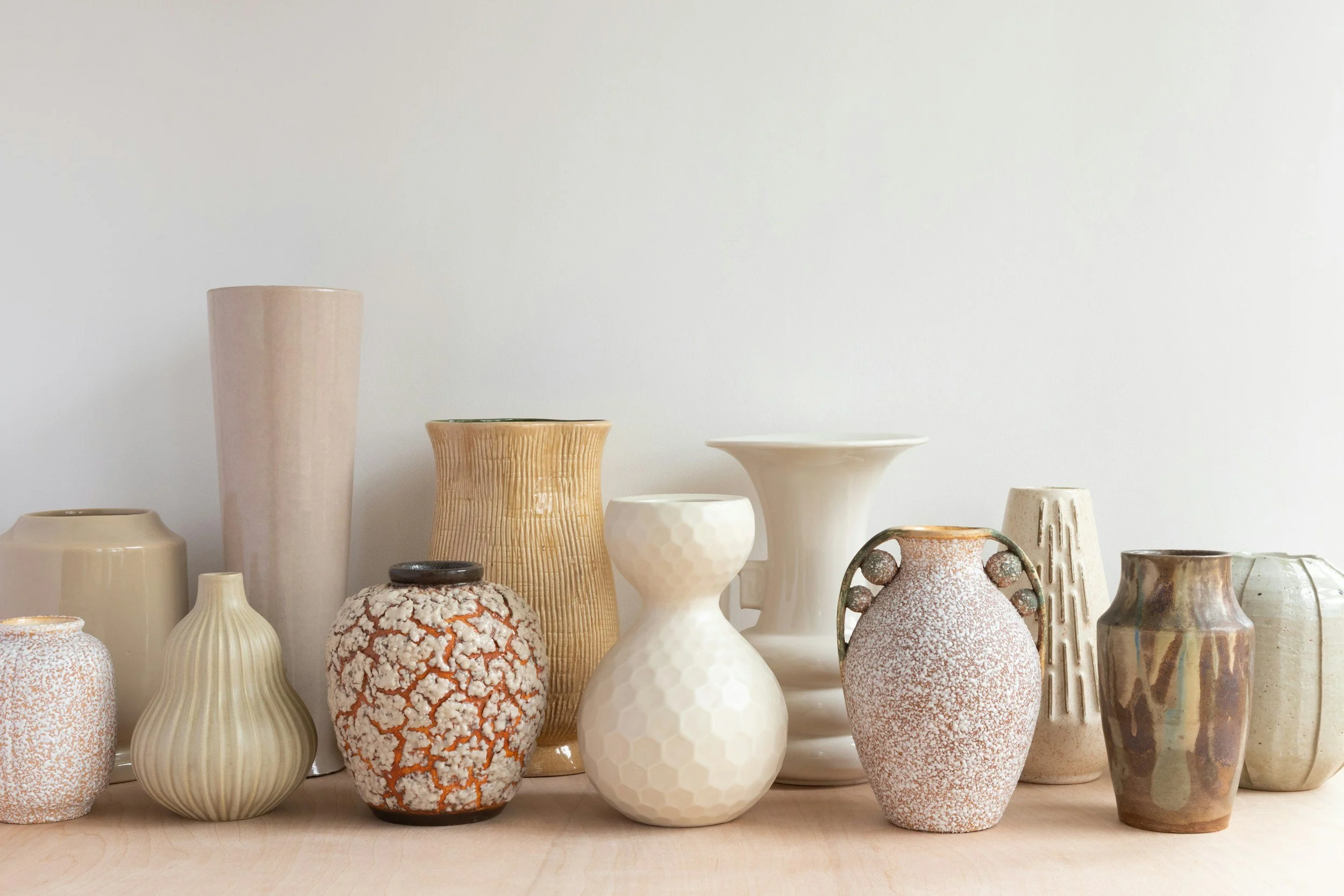 Collection of various ceramic vases in neutral tones on a wooden surface.