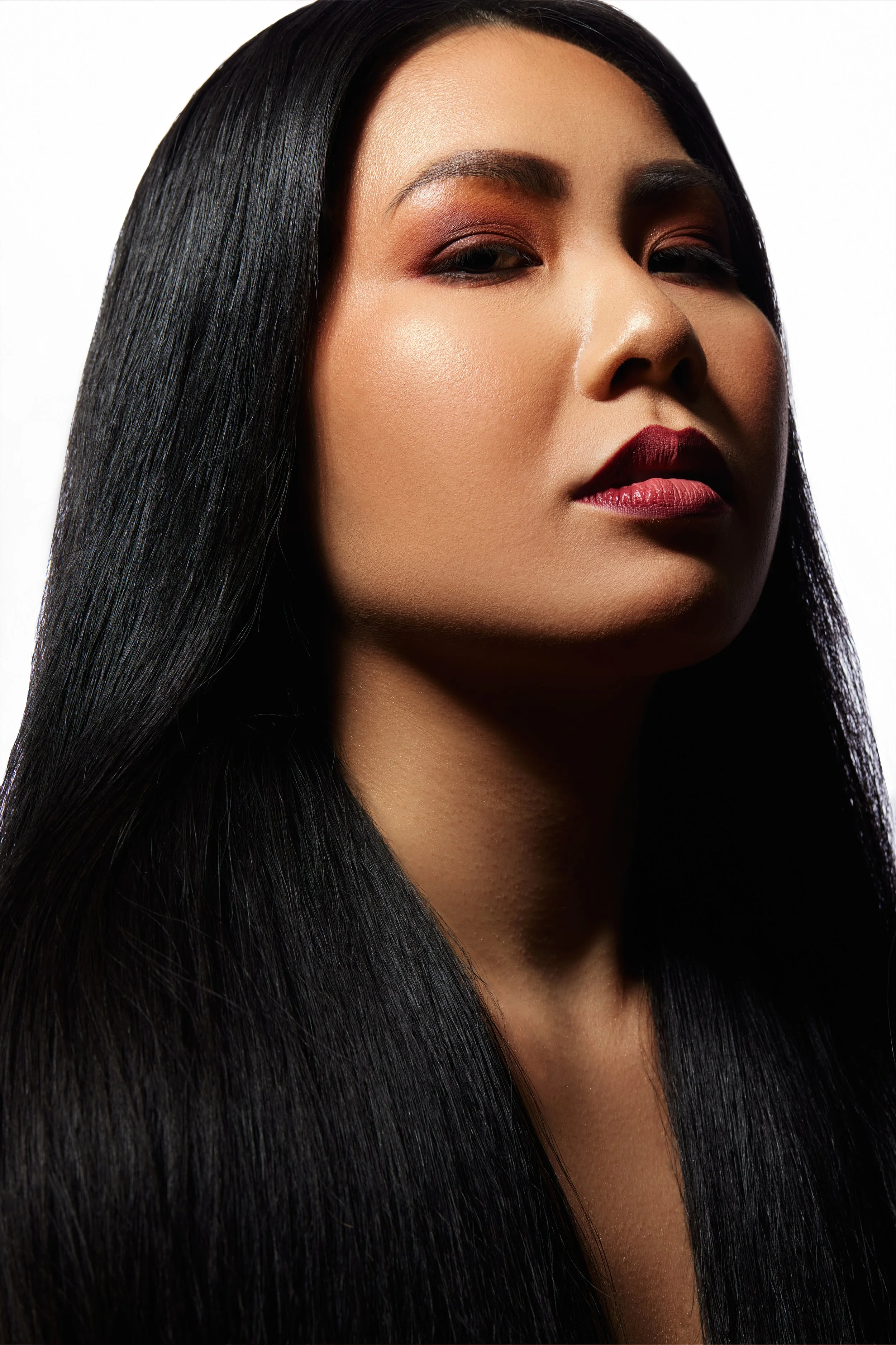 A woman with long, straight black hair, wearing makeup with bold lipstick and eyeshadow, looking slightly to the side.