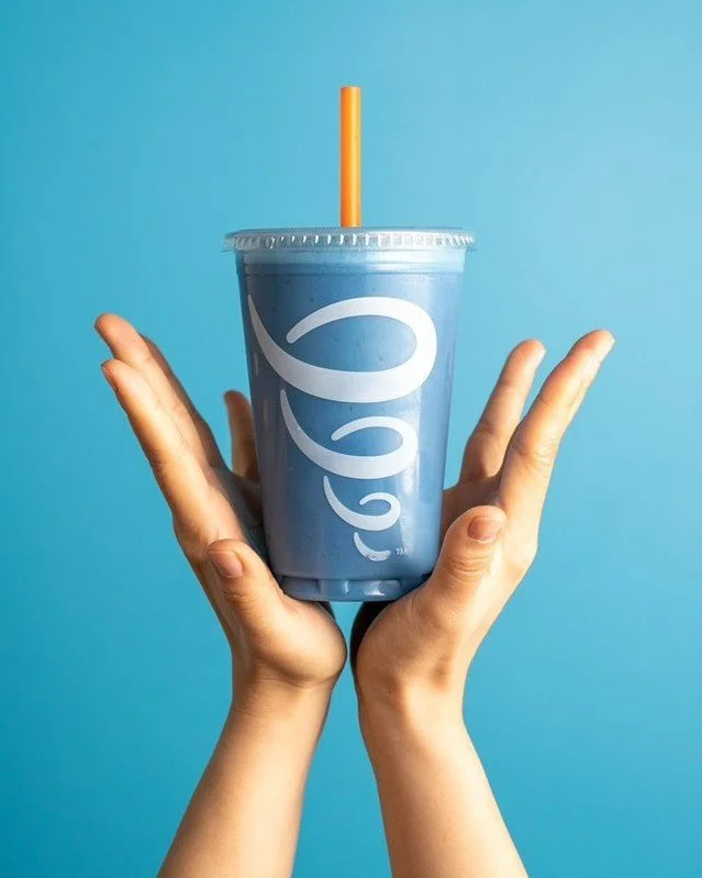 Two hands hold a large blue milkshake with a straw against a blue background.