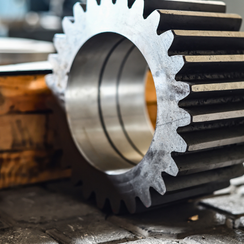 Close-up of a large metal gear with worn teeth, resting on a workbench.