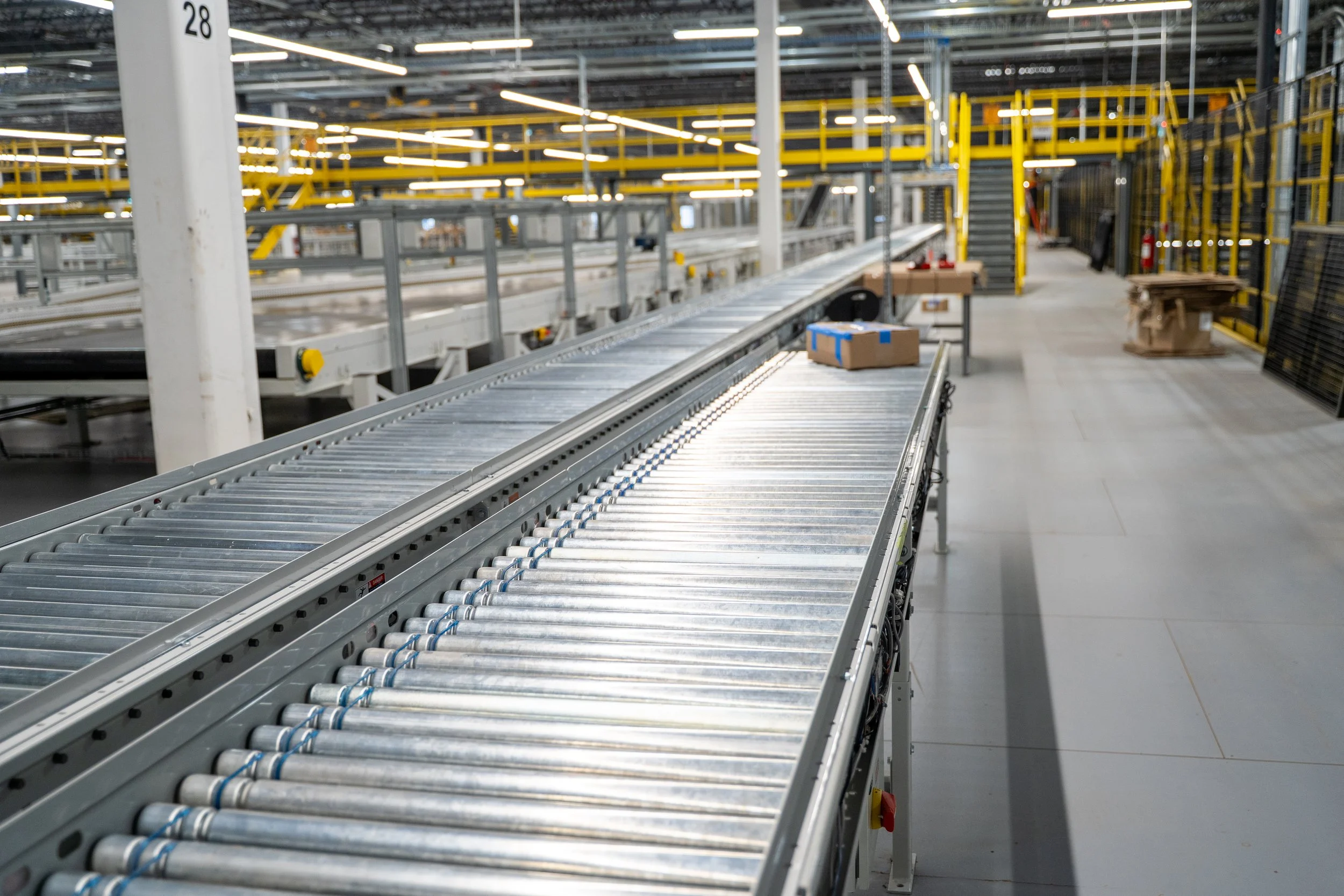Empty industrial warehouse with conveyor belts and yellow safety railings.