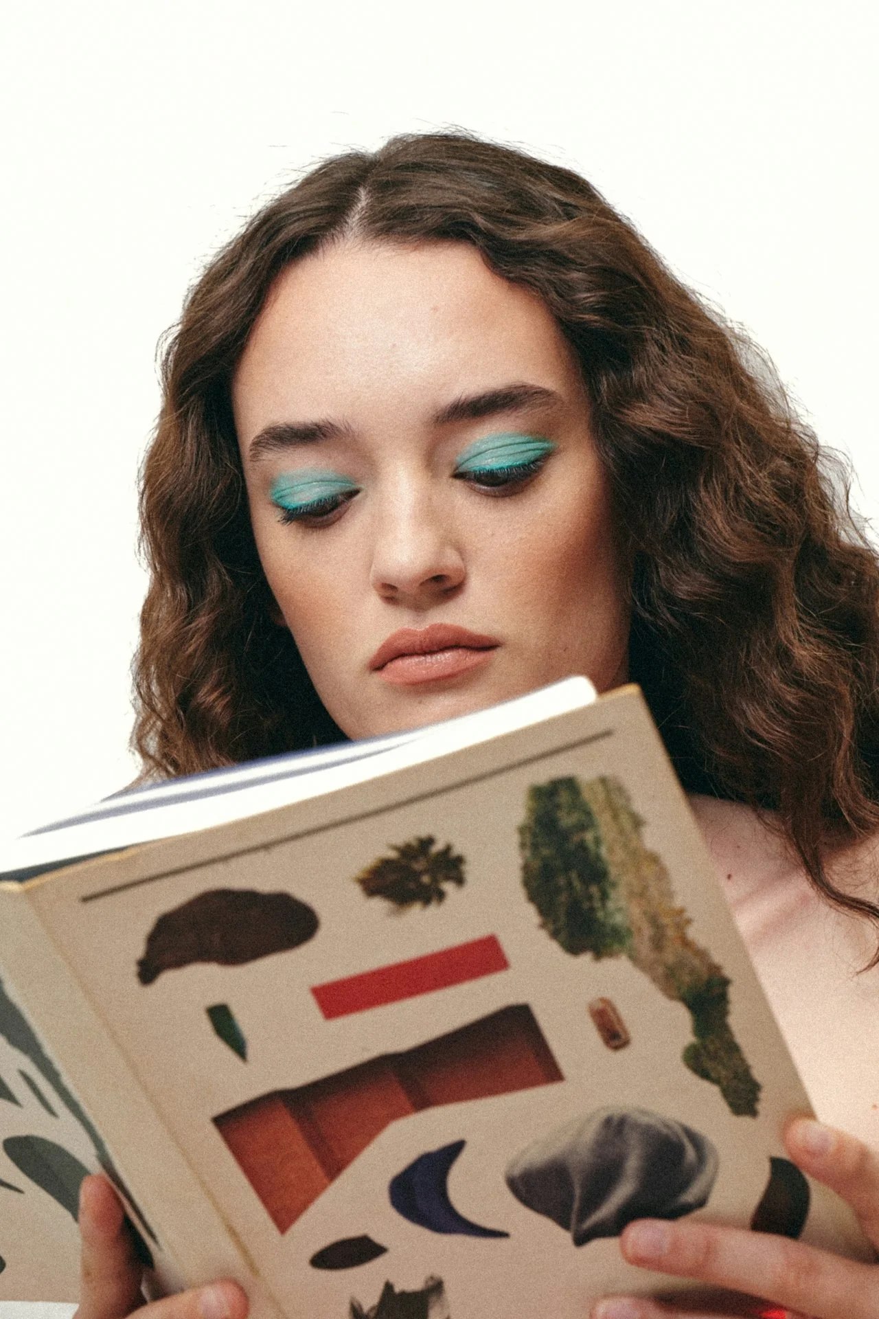 Person with blue eyeshadow reading a book with abstract art on the cover.