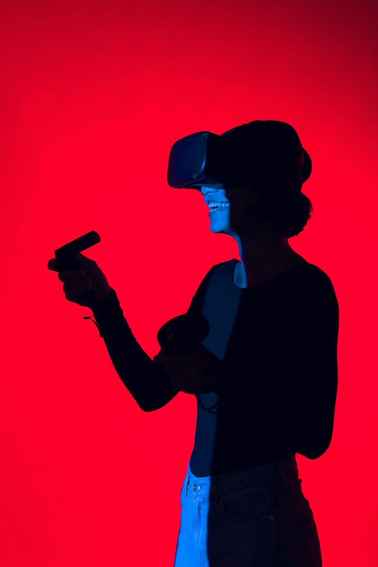 Person wearing a virtual reality headset and holding controllers, silhouetted against a red background.