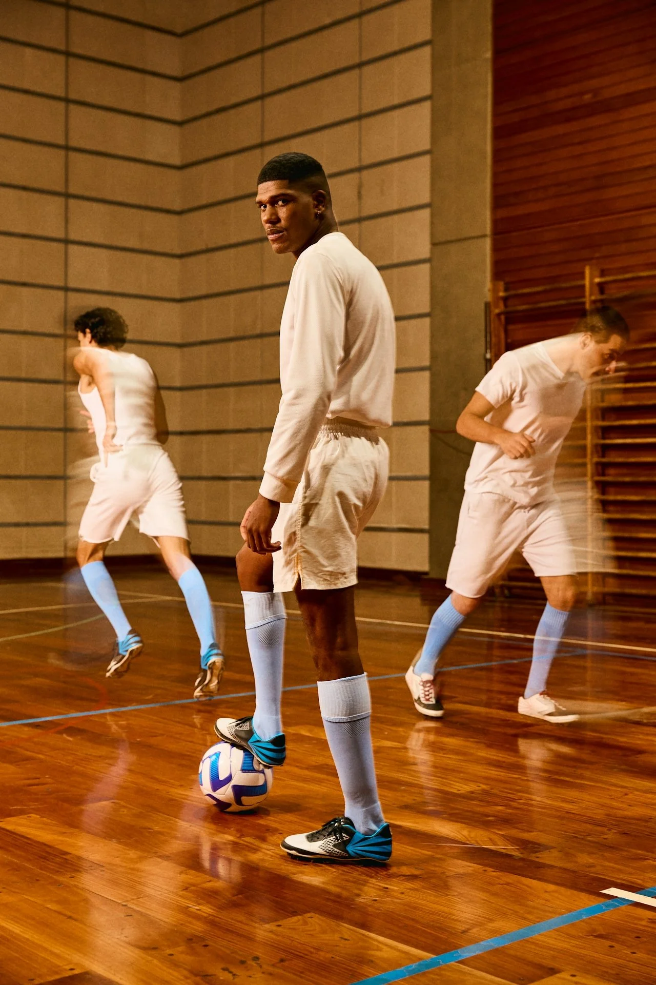Indoor soccer players in white uniforms and light blue socks practicing on a wooden court.