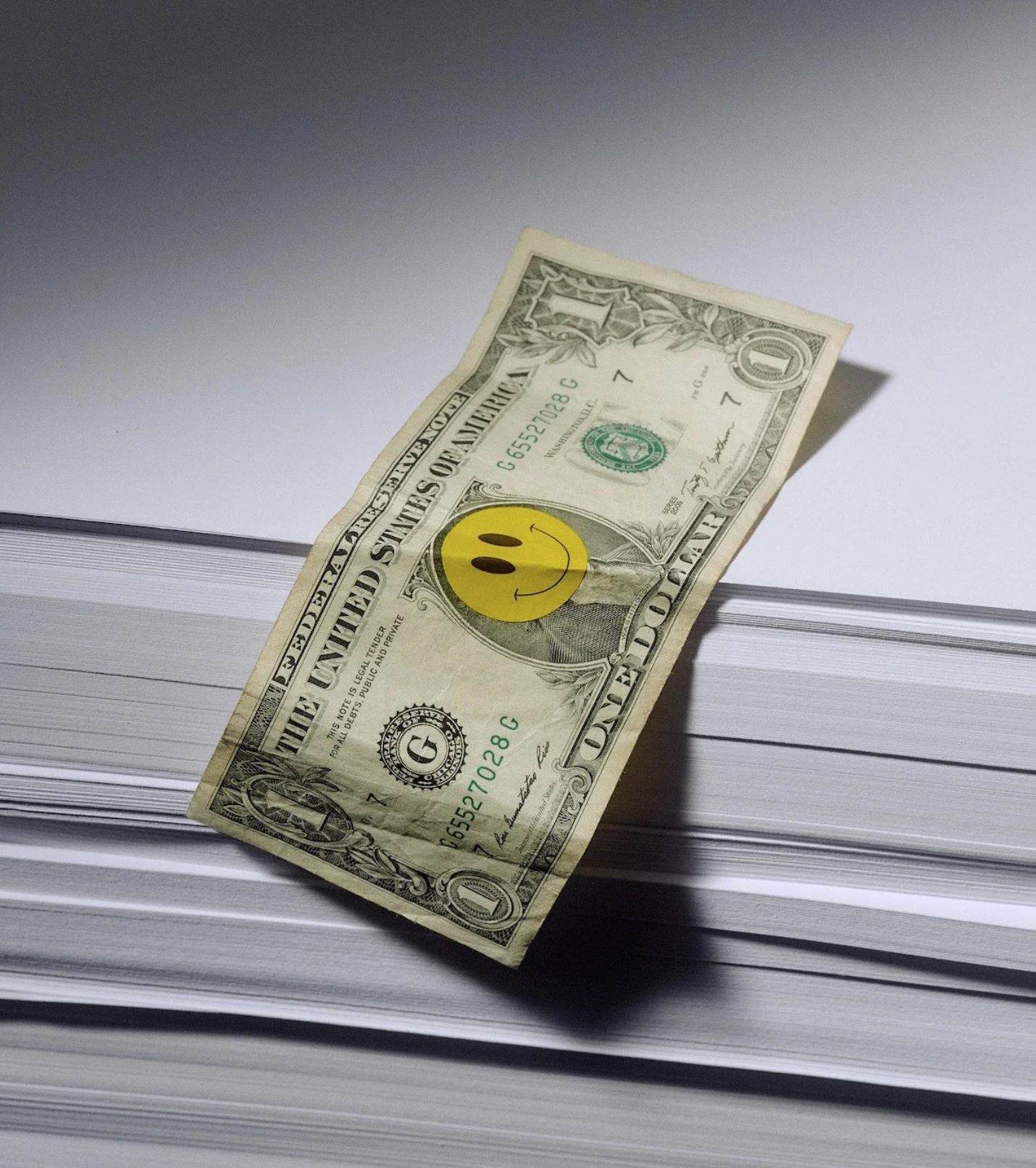 One dollar bill with a yellow smiley face sticker on a stack of paper