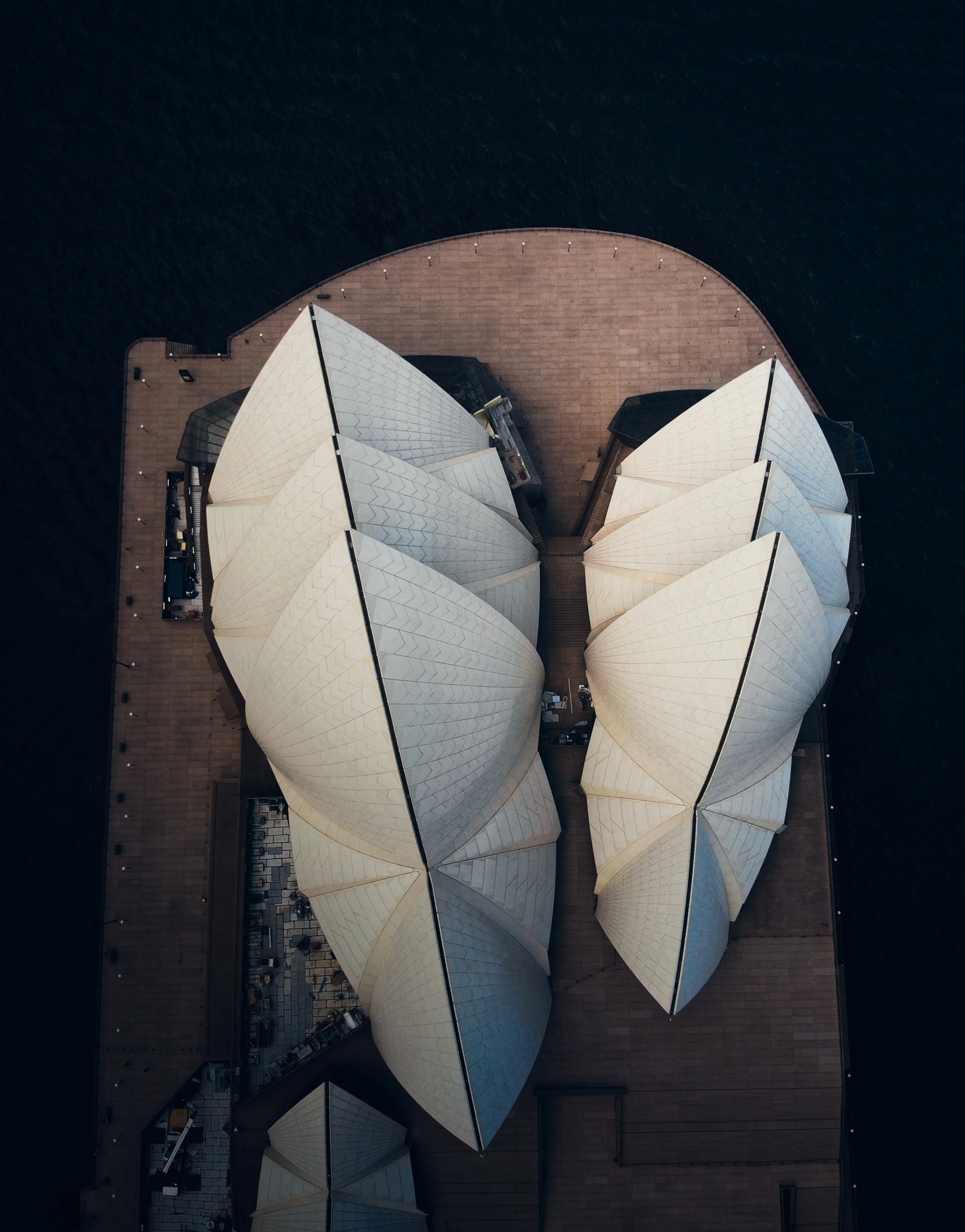 Aerial view of the Sydney Opera House with its iconic white sail-shaped roofs and surrounding platform area.
