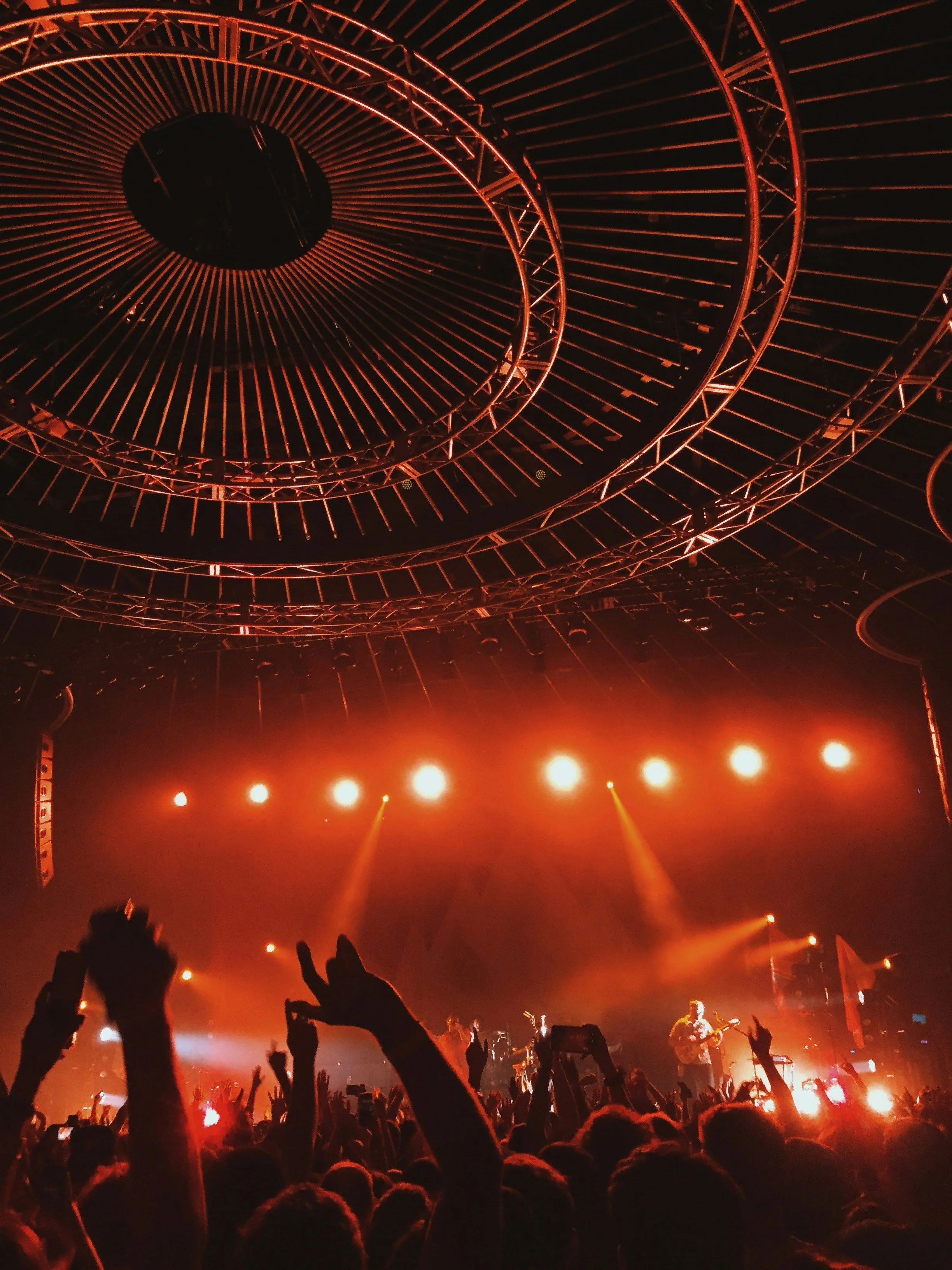 Concert stage with bright orange lighting, circular ceiling structure, and crowd with raised hands