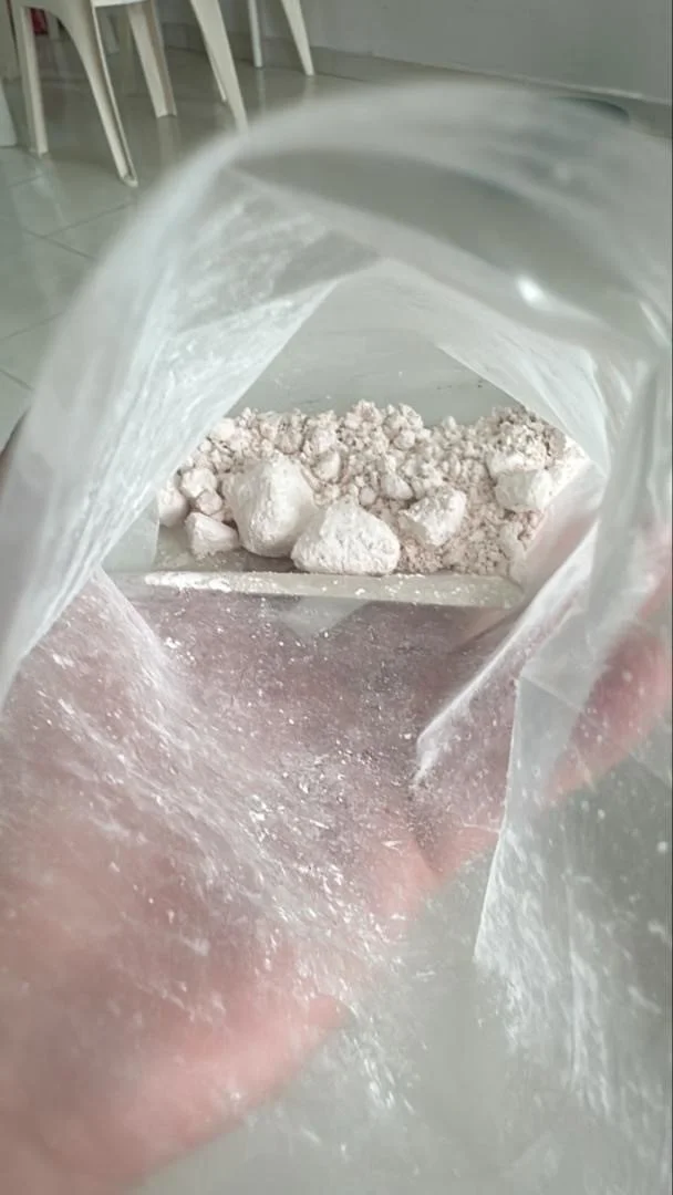 A plastic bag held open, revealing white powdery rare earth carbonate and larger clumps inside.