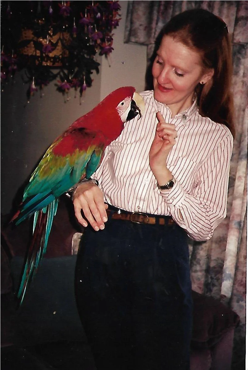 young lady in white top and black bottoms holding parrot on arm