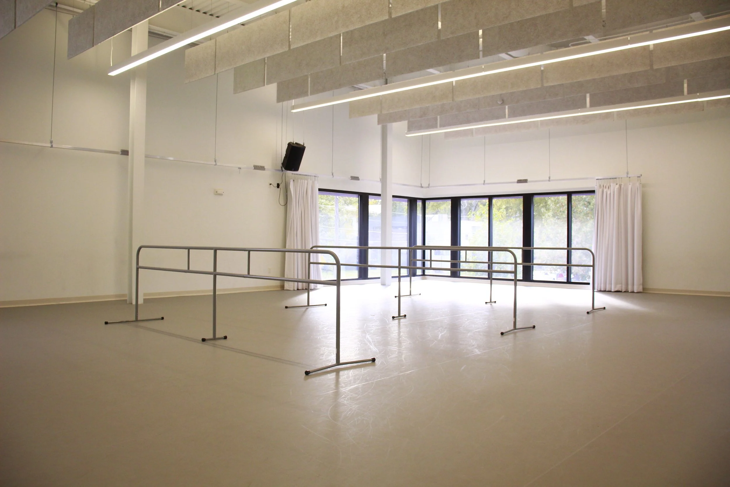 Empty dance studio with large windows, white curtains, and ballet barres