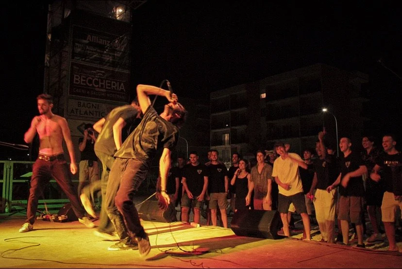 Band performing on stage at night with audience watching and cheering.