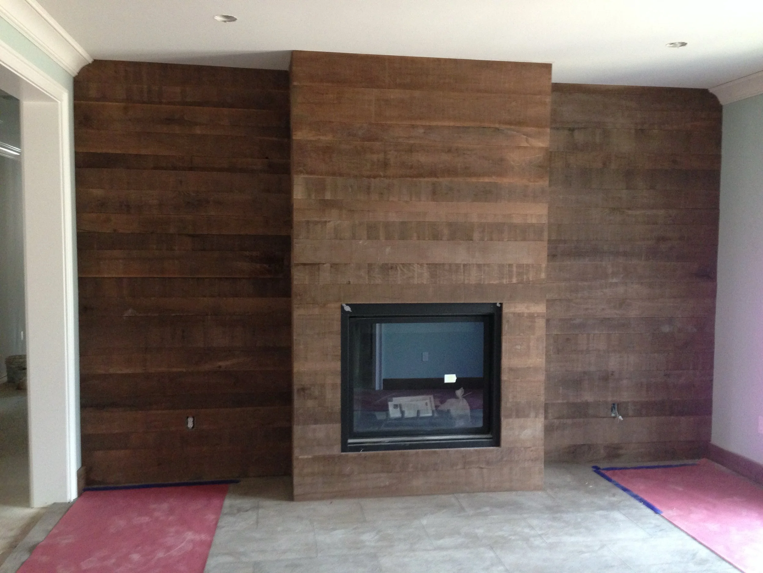 Wood-paneled wall with a centered fireplace, a brick-red mat on the floor in front of the wall, and a partially visible doorway with a white frame on the left.
