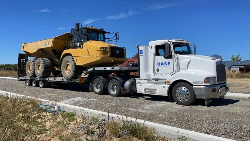 A semi-truck transporting a large yellow construction vehicle on a flatbed trailer.