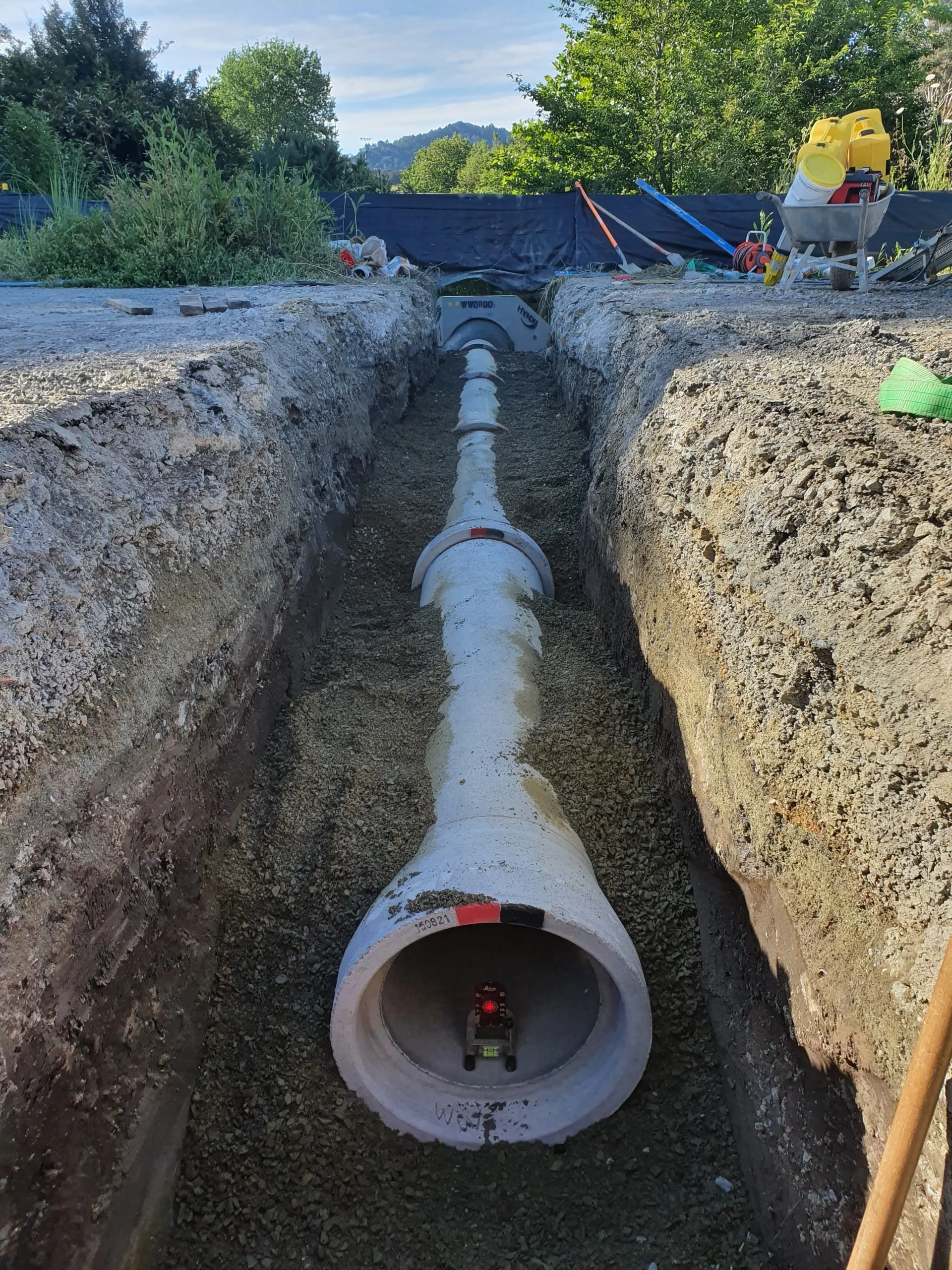 Installation of underground pipe in a trench for utility or drainage system, with construction tools and materials nearby.
