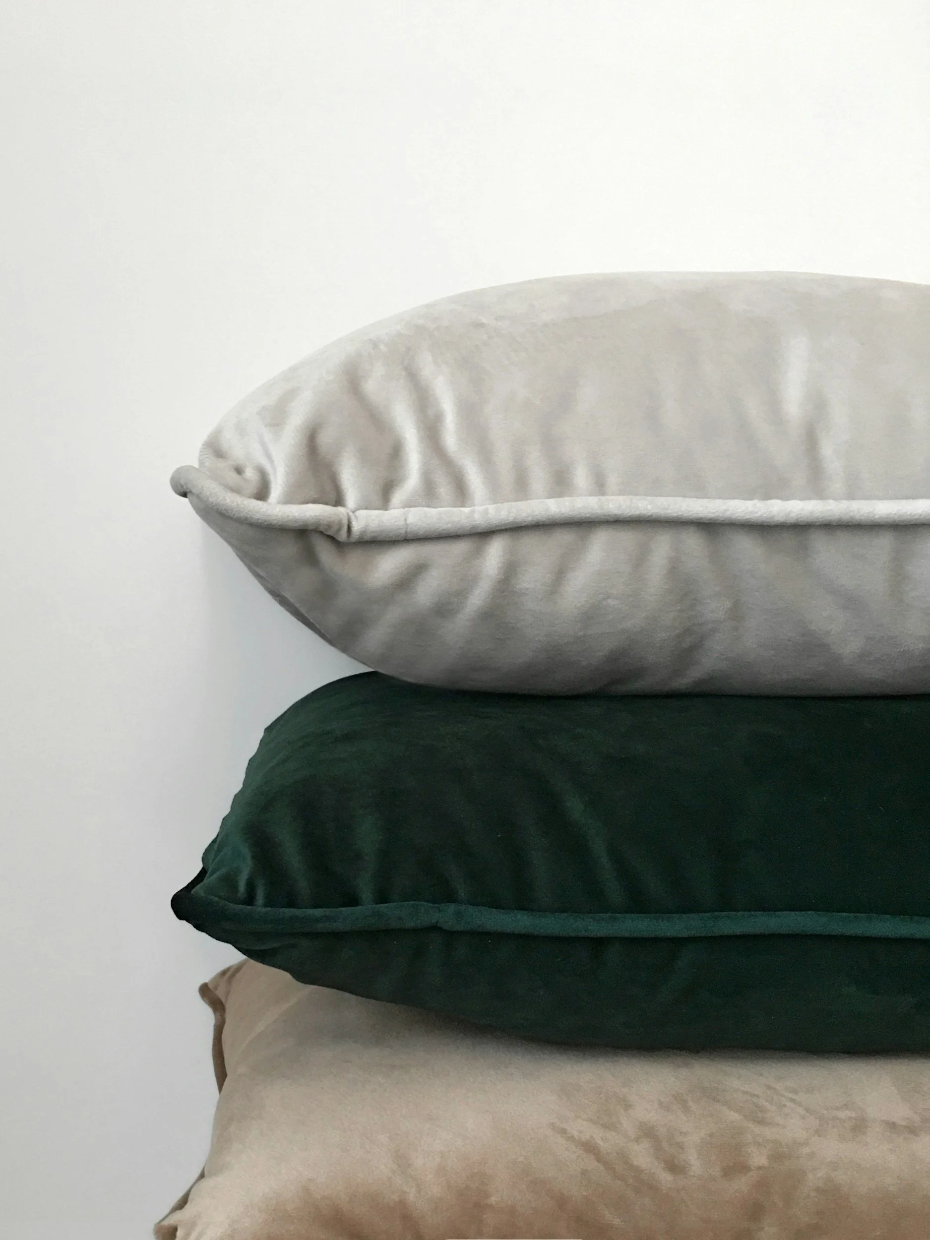 Stacked pillows in neutral and dark green colors against a plain white wall.