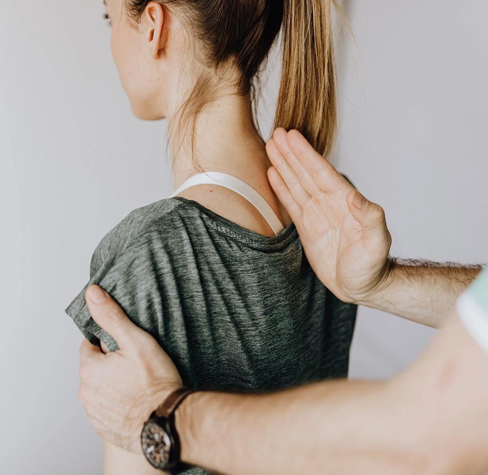 A person receiving a physical examination or physical therapy, with a care provider placing their hand on the person's shoulder and neck, and the person holding their shoulder.