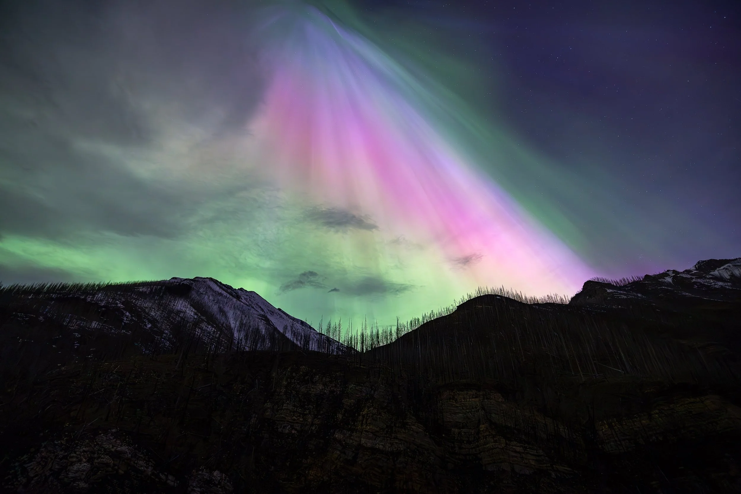 Night sky illuminated by colorful aurora borealis over mountain ridges.