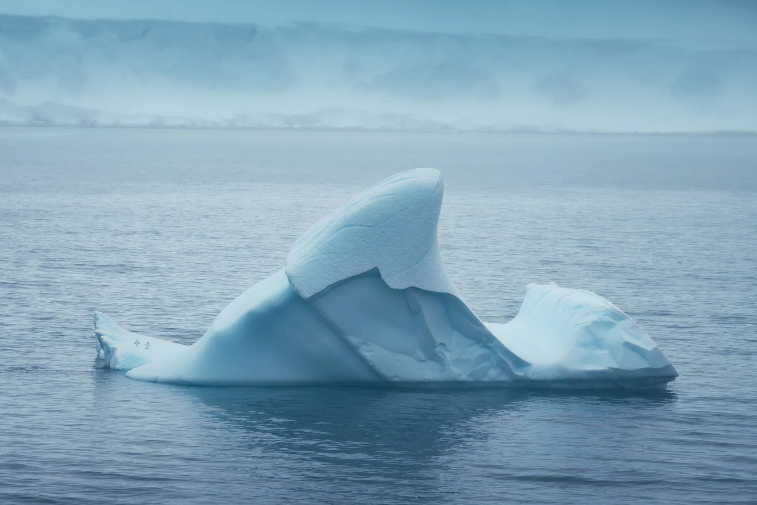 A large iceberg floating in the ocean with a cloudy sky in the background.