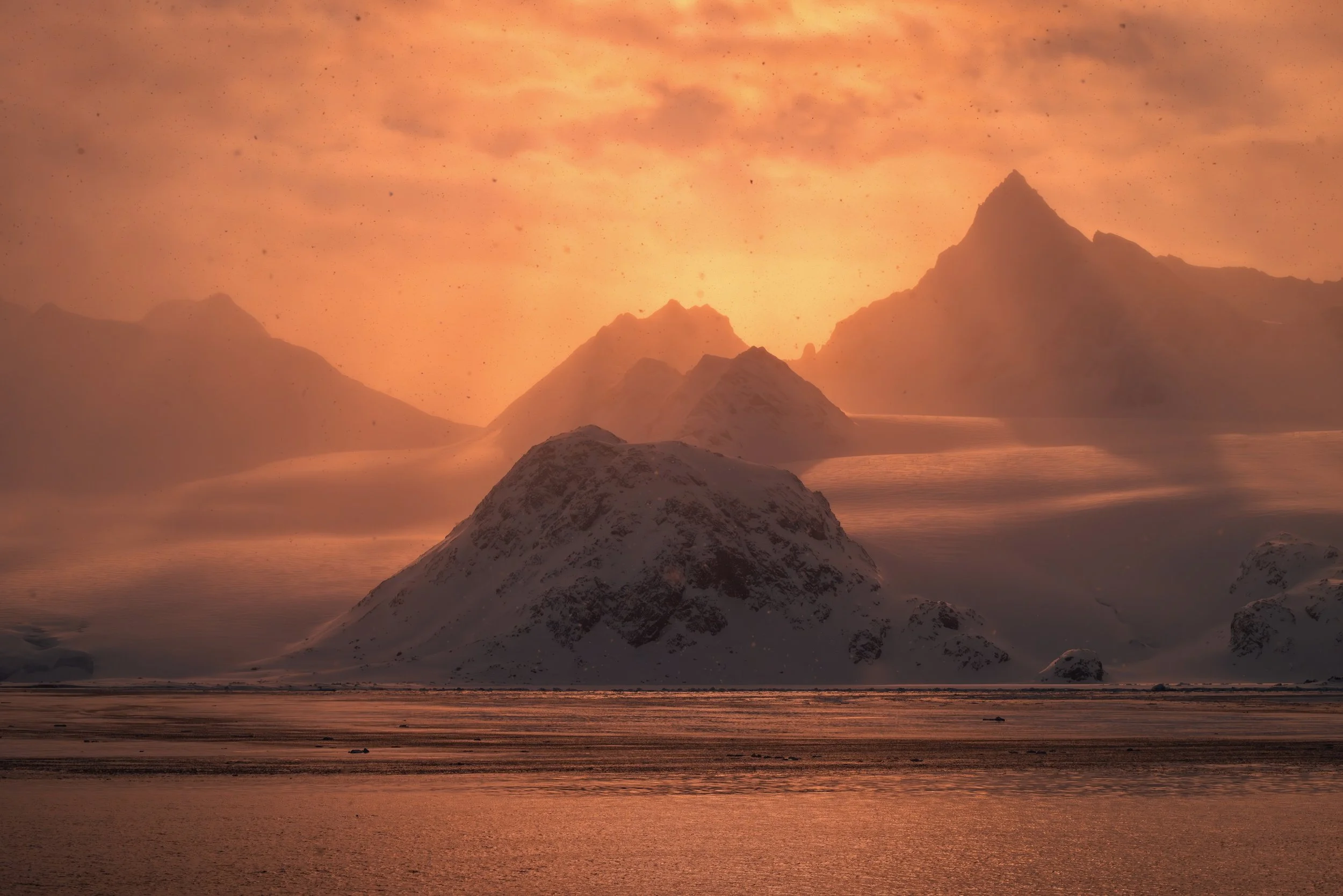 Snow-covered mountain peaks at sunset or sunrise with a reddish-orange sky.
