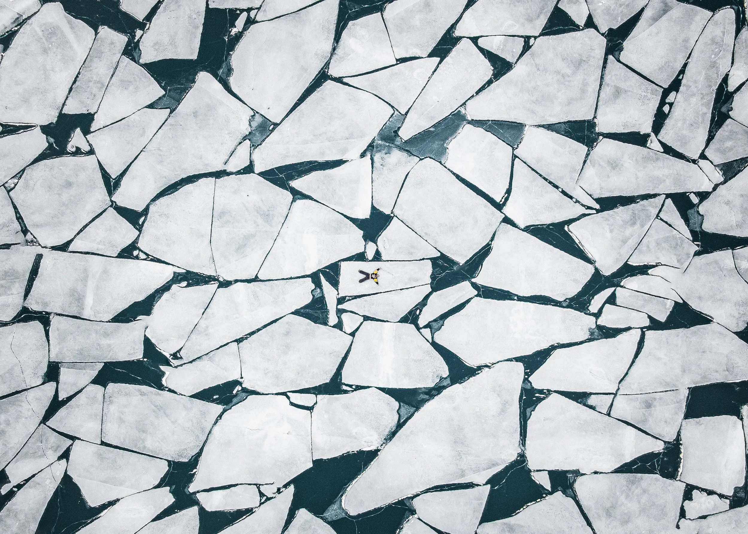 A cracked ice surface with a person laying in the center.
