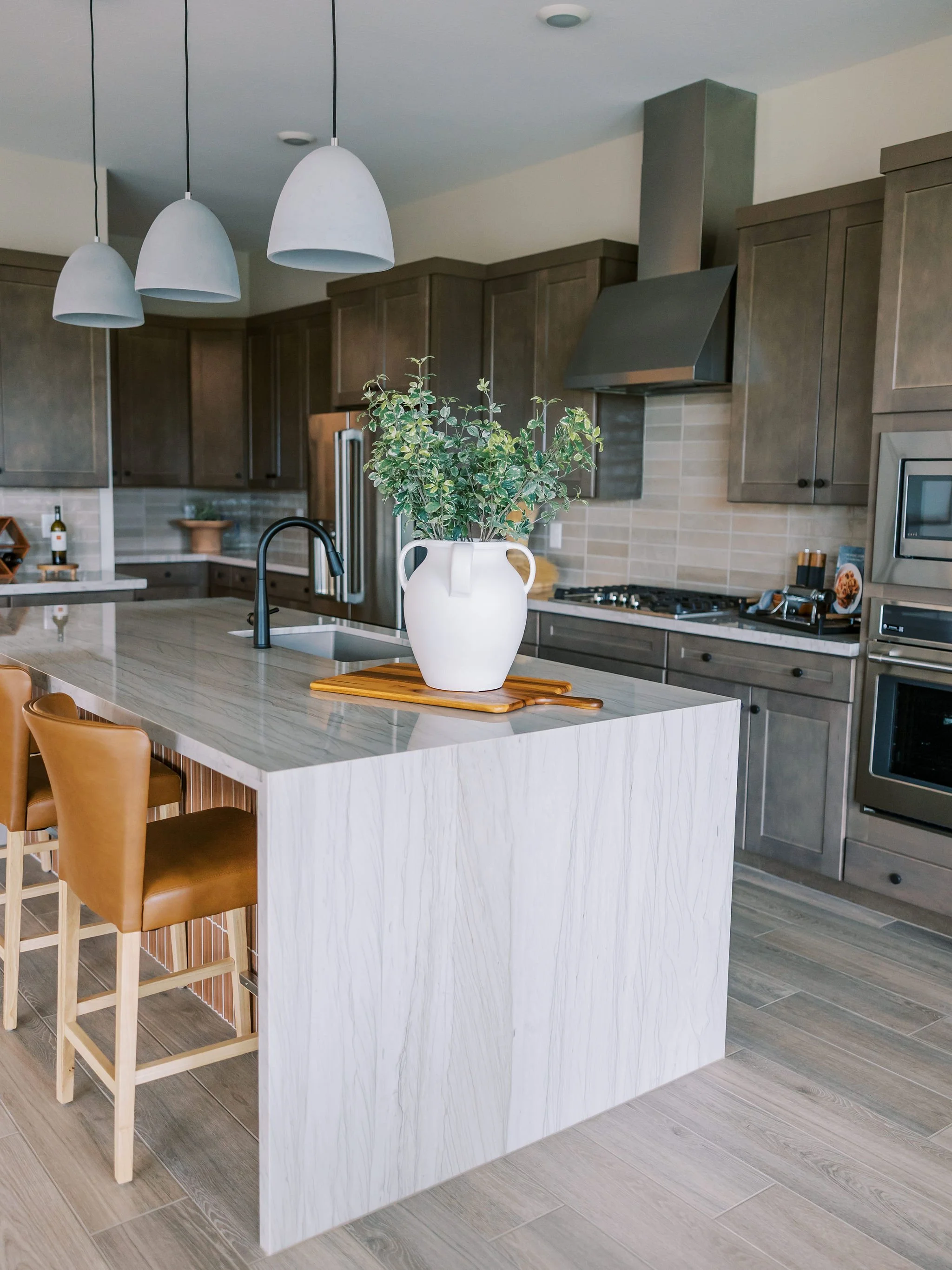 Modern kitchen with gray cabinets, a white marble island, three pendant lights, and a potted plant on the island.