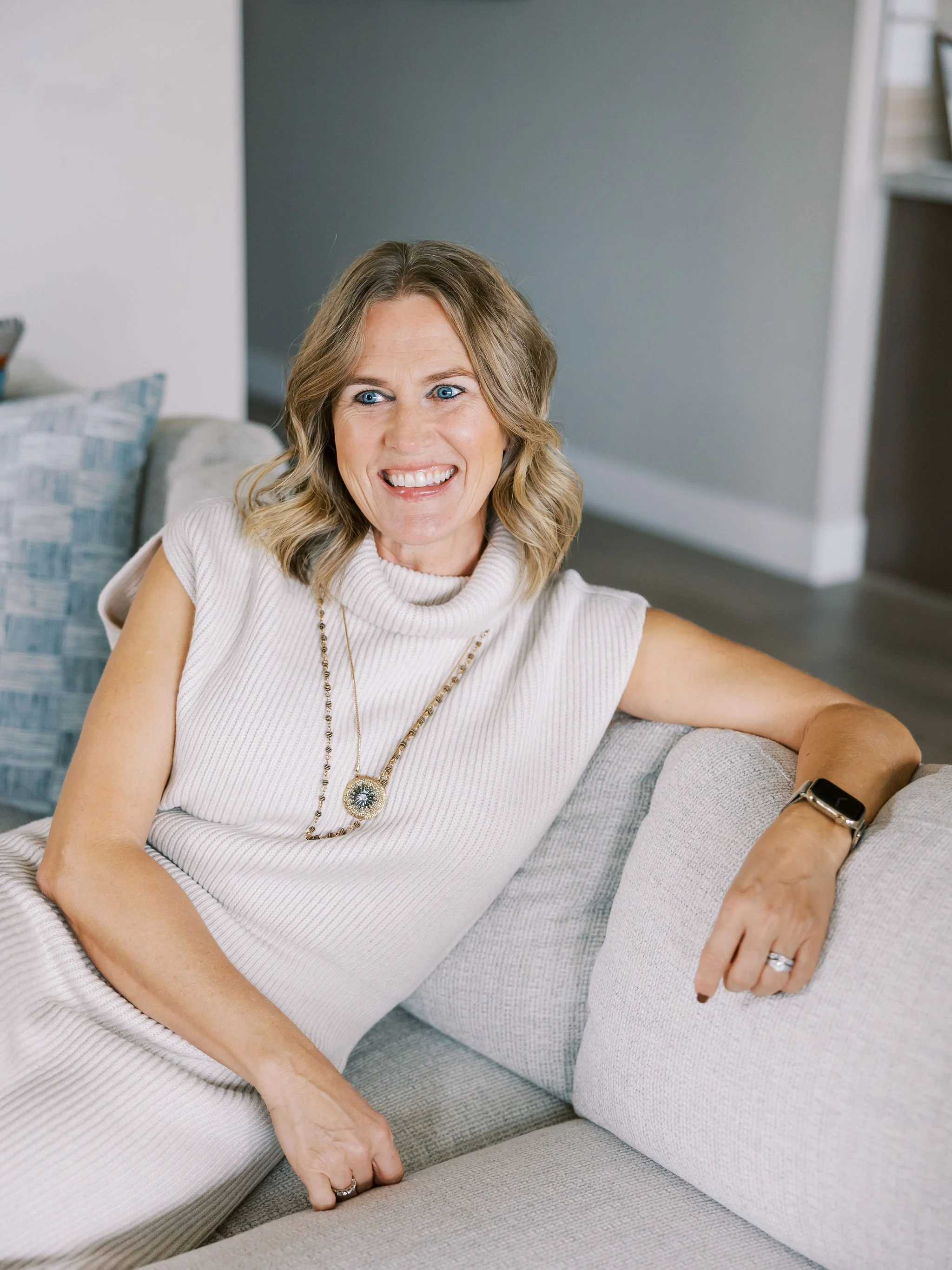 Jessica Curtis sitting on a light-colored sofa in a modern living room.