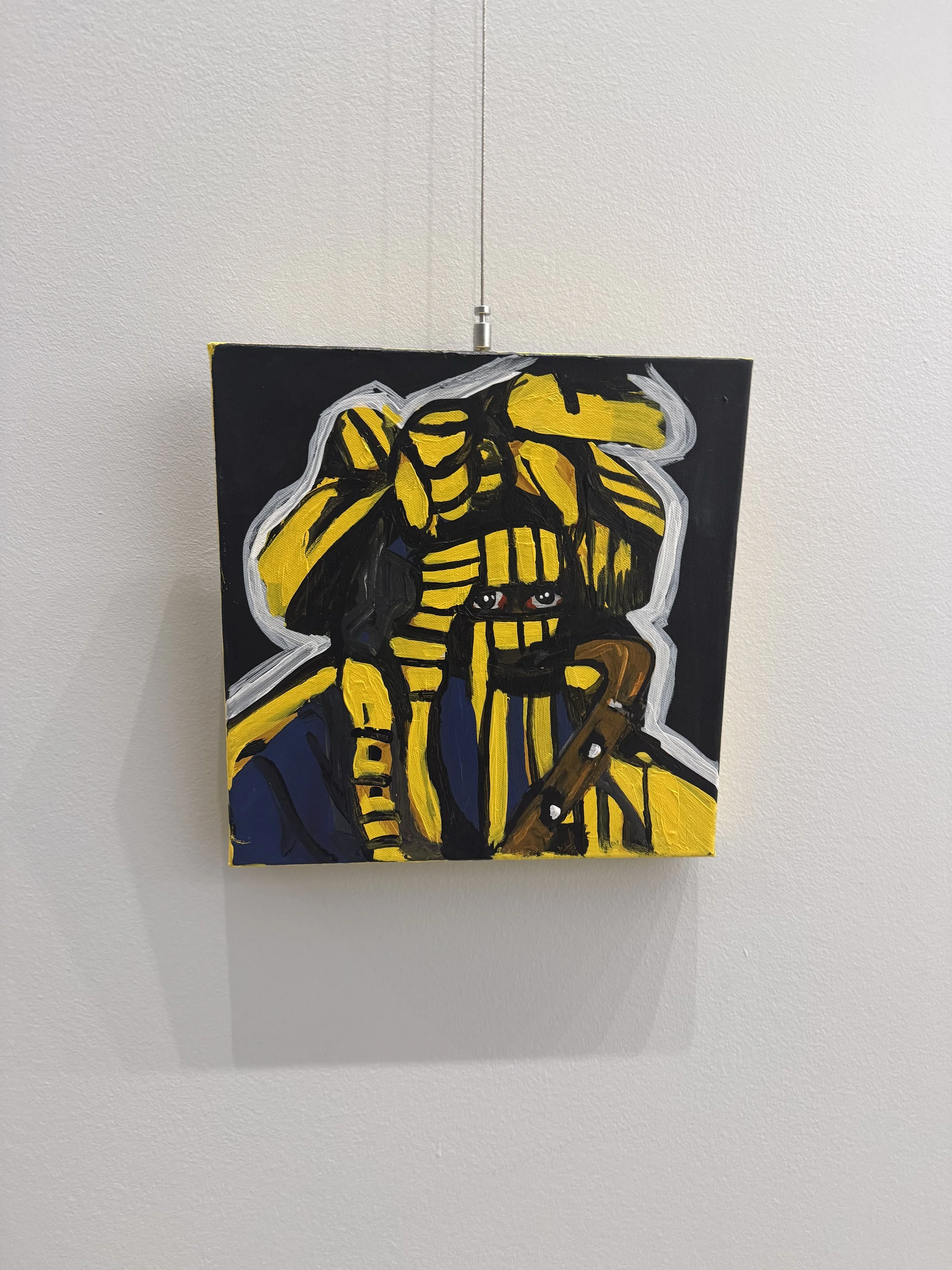 Abstract painting of a figure wearing a striped yellow and black headpiece and clothing, with vivid colors and bold brushstrokes, mounted on a white wall.
