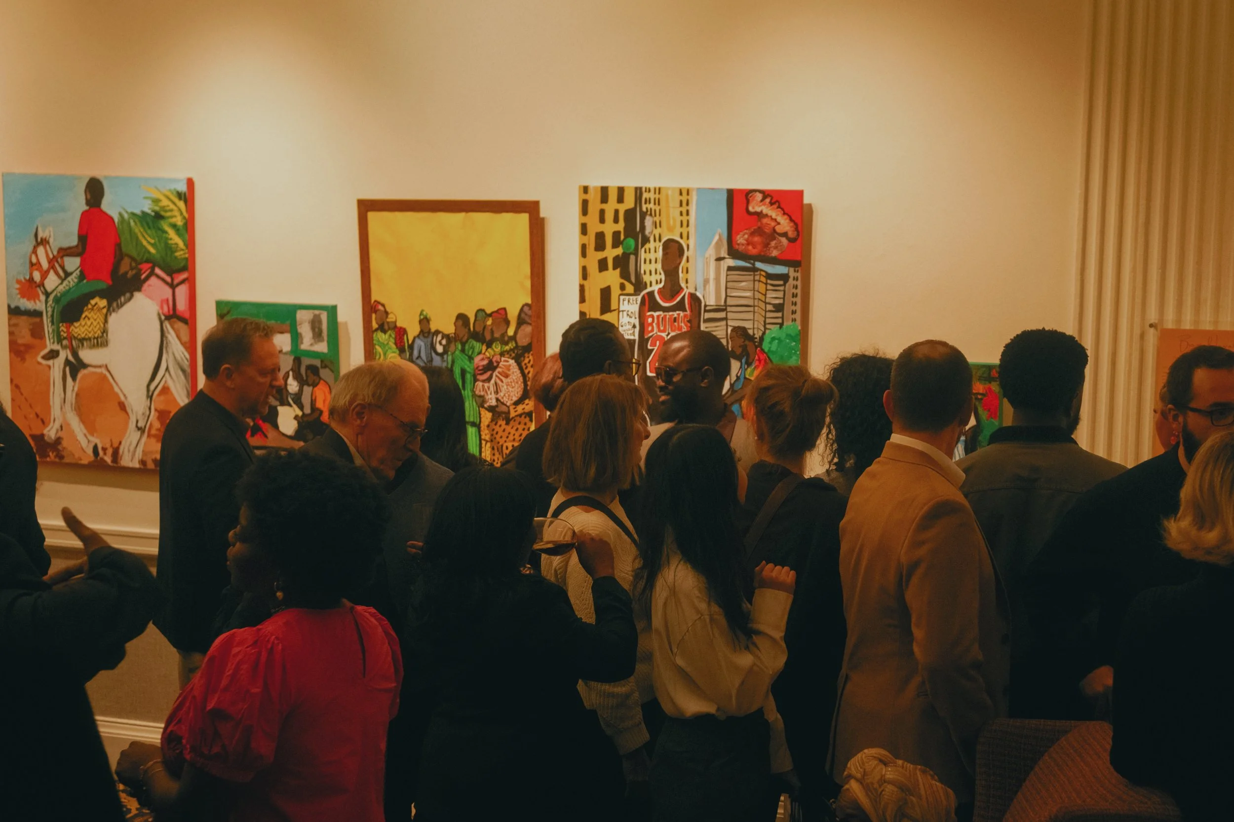 A group of people gathered in an art gallery, viewing colorful paintings on the walls.