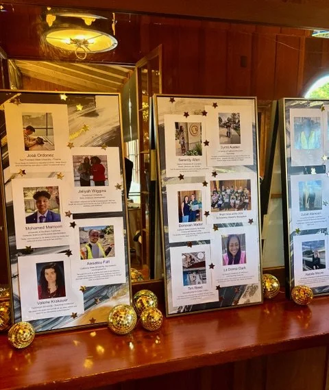 Three large presentation boards with photographs and names of children, decorated with small star and globe ornaments, placed on a polished wooden surface inside a wooden-paneled room.