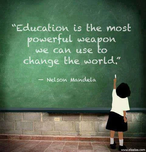 A girl in a white shirt and black skirt standing in front of a green chalkboard writing a quote from Nelson Mandela about education being the most powerful weapon to change the world.