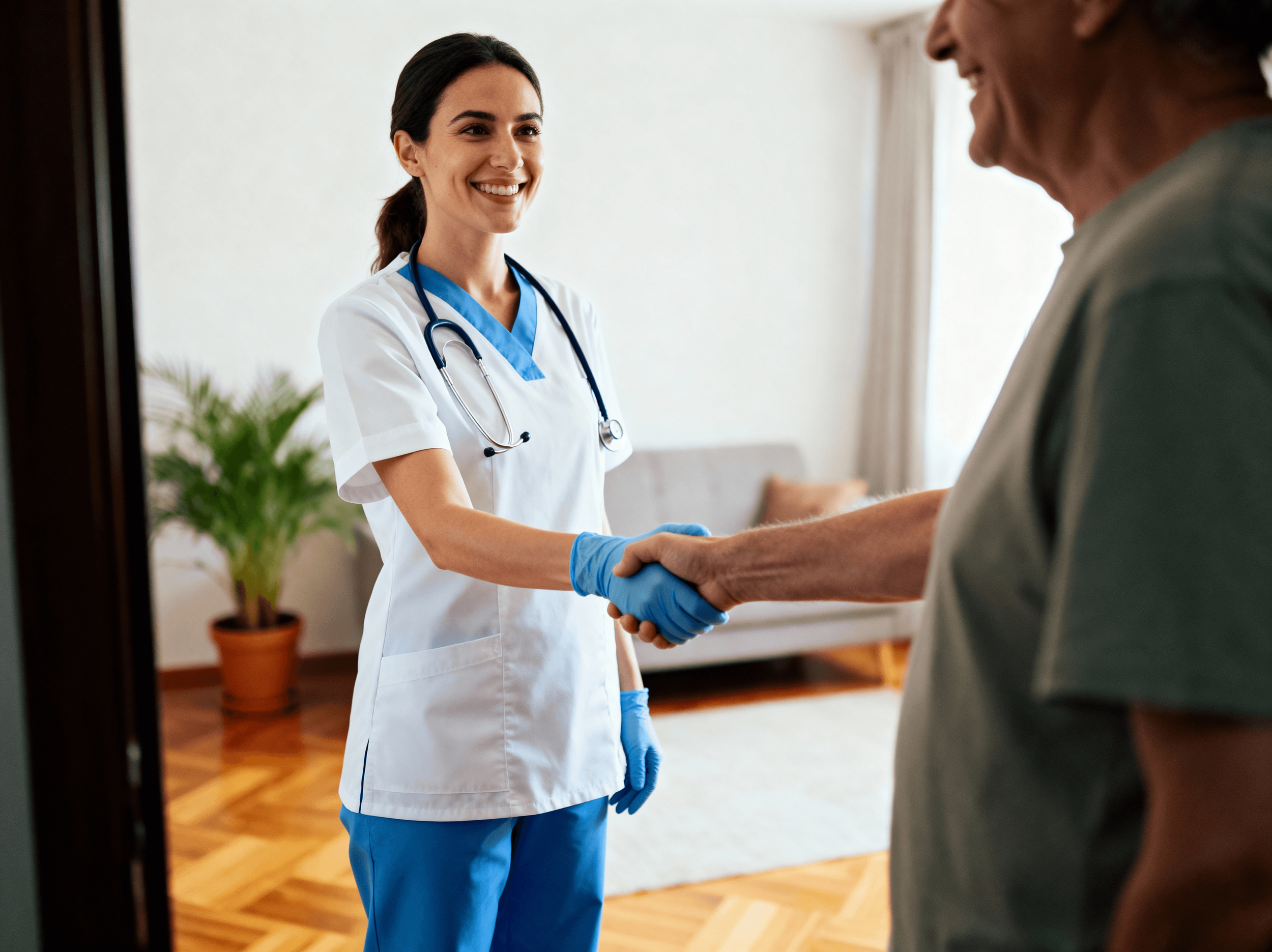A nurse in white scrubs with a stethoscope around her neck hands an elderly patient a handshake, smiling at each other inside a well-lit room.