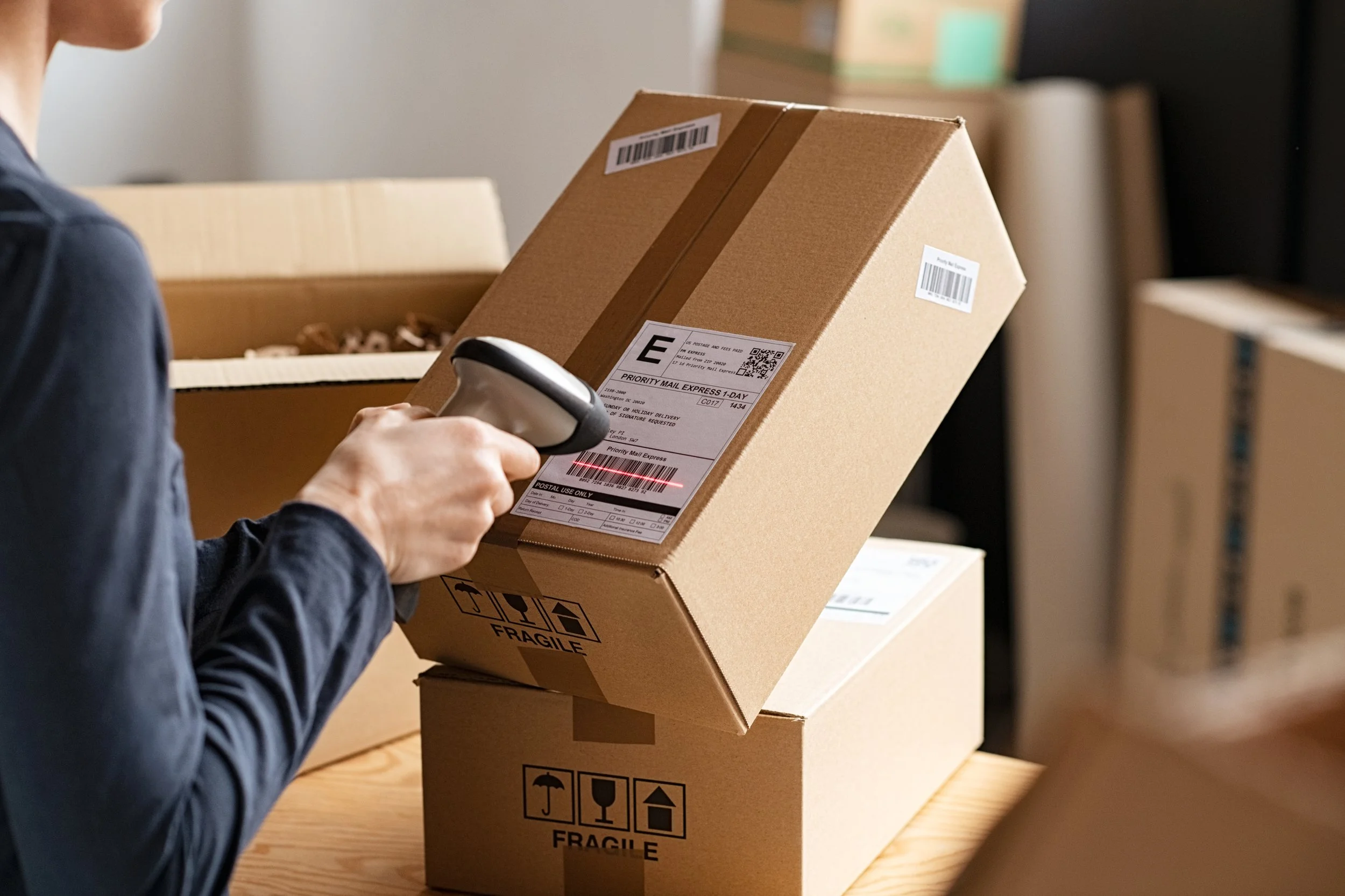 A person scanning a shipping label on a cardboard box at a packing or warehouse facility.
