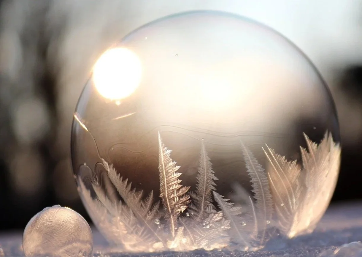 Gefrorene Wassertropfen in Form von Schneeflocken auf einer Eisblase im Sonnenlicht, Schnee im Vordergrund.