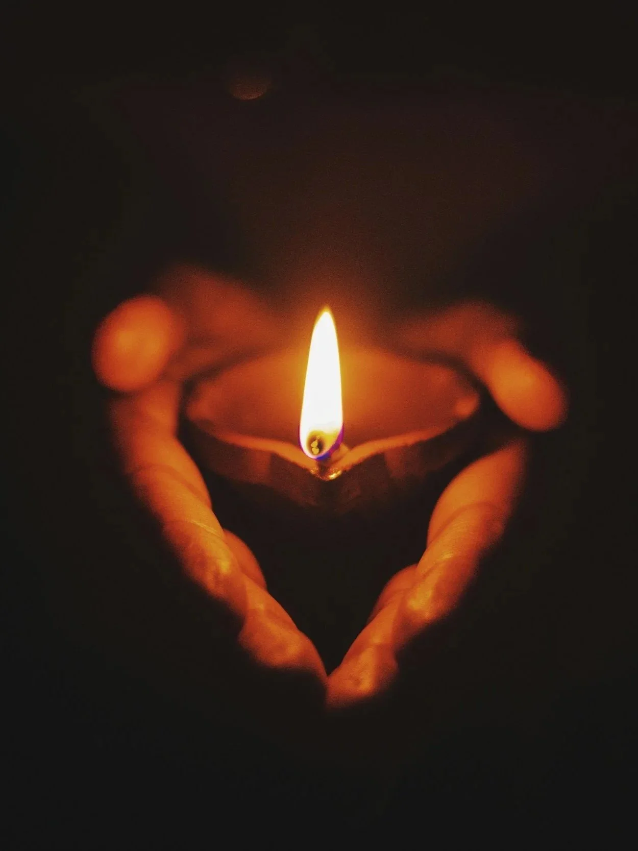 Person holding a lit candle in a small decorative holder, the flame illuminating the dark surrounding with a warm glow.