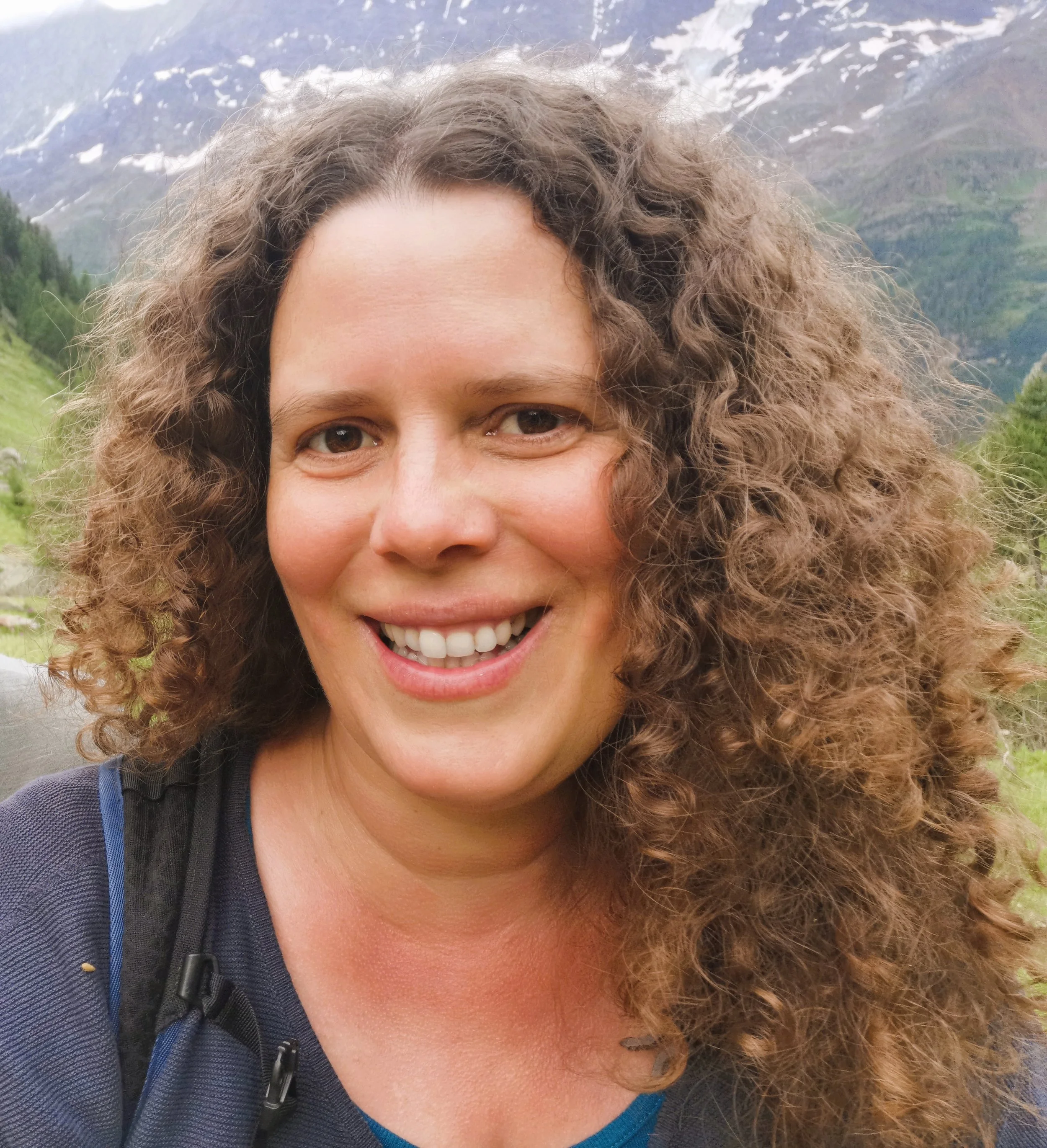 Lächelnde Frau mit Locken vor Berglandschaft und Schnee am Gipfel