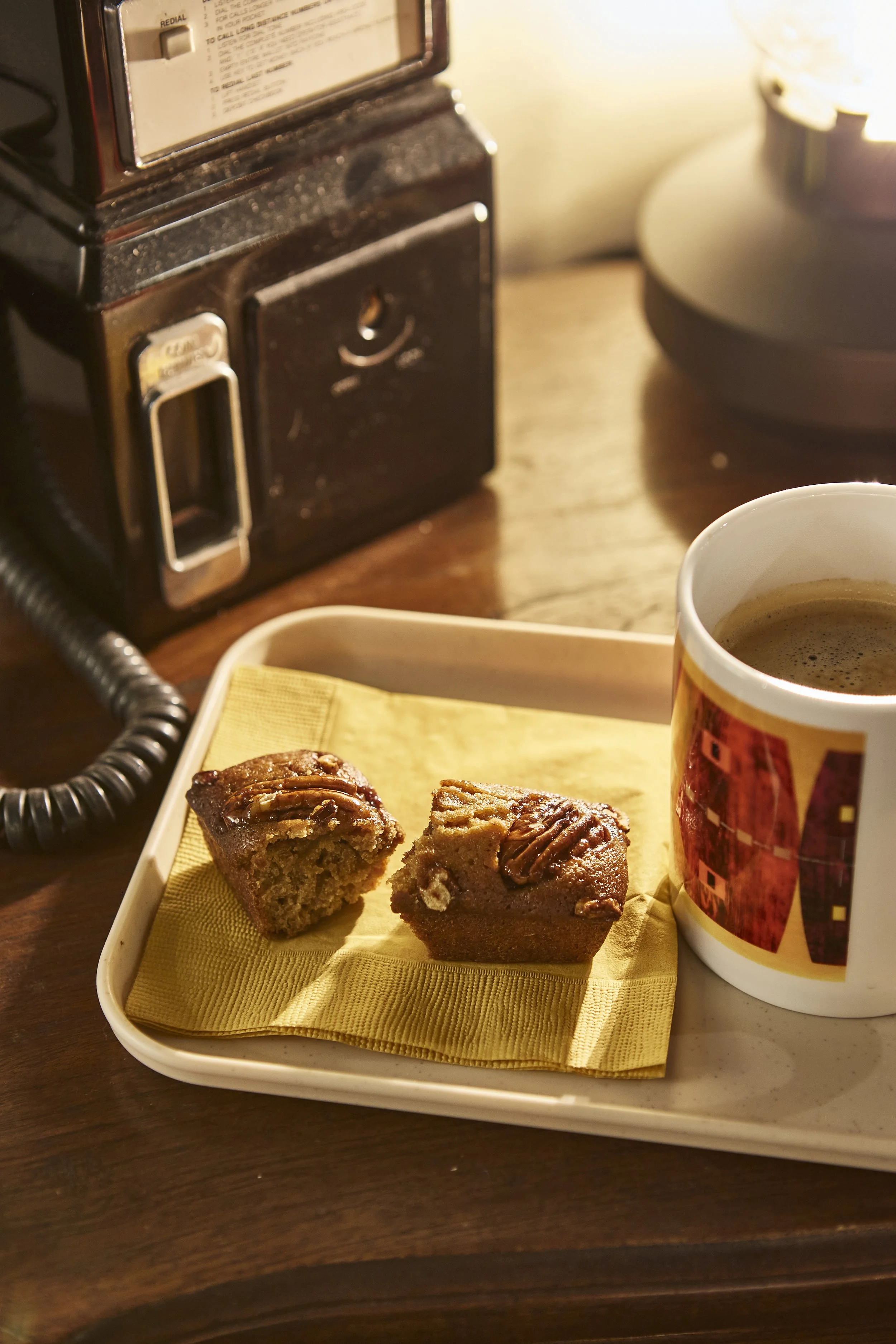 커피 한 잔과 쿠키 두 조각이 담긴 트레이, 배경에 오래된 전화기와 램프가 있는 책상 모습.