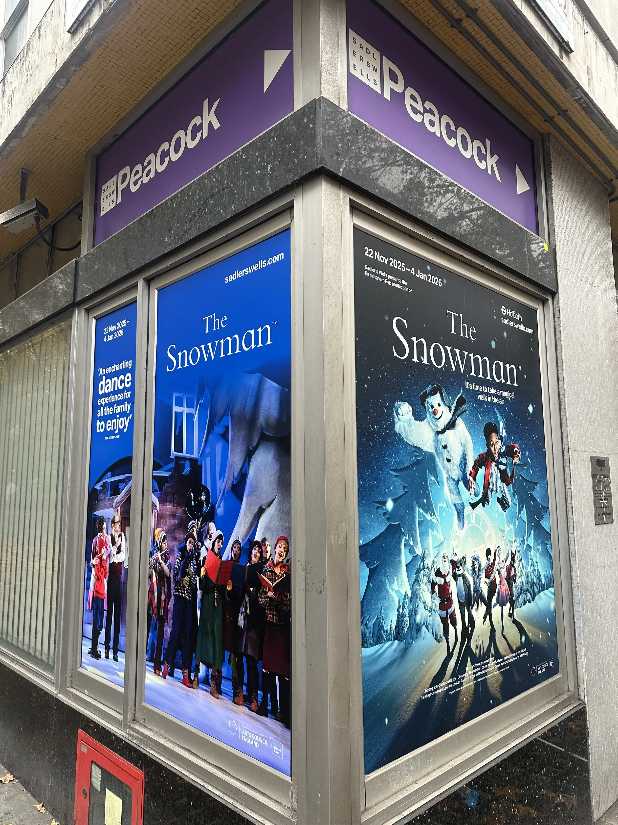 window graphics with advertisements for the show 'The Snowman' on the corner of a building, featuring a winter scene with a snowman and children.