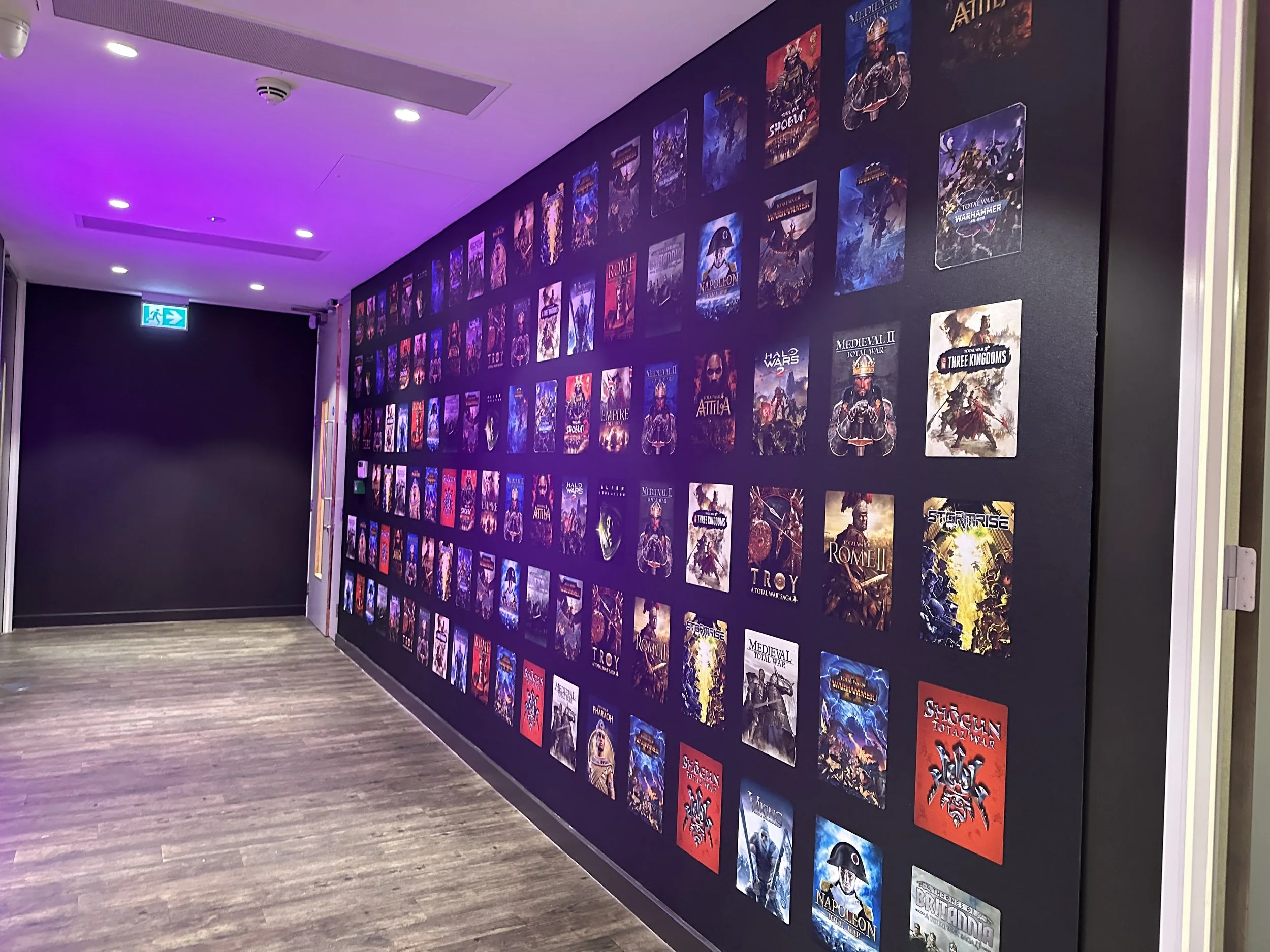 A one piece wallpaper covered with various video game or movie posters, featuring titles like 'Medieval II', 'Rome', 'Napoleon', 'Total War', and others, in a room with purple ambient lighting.
