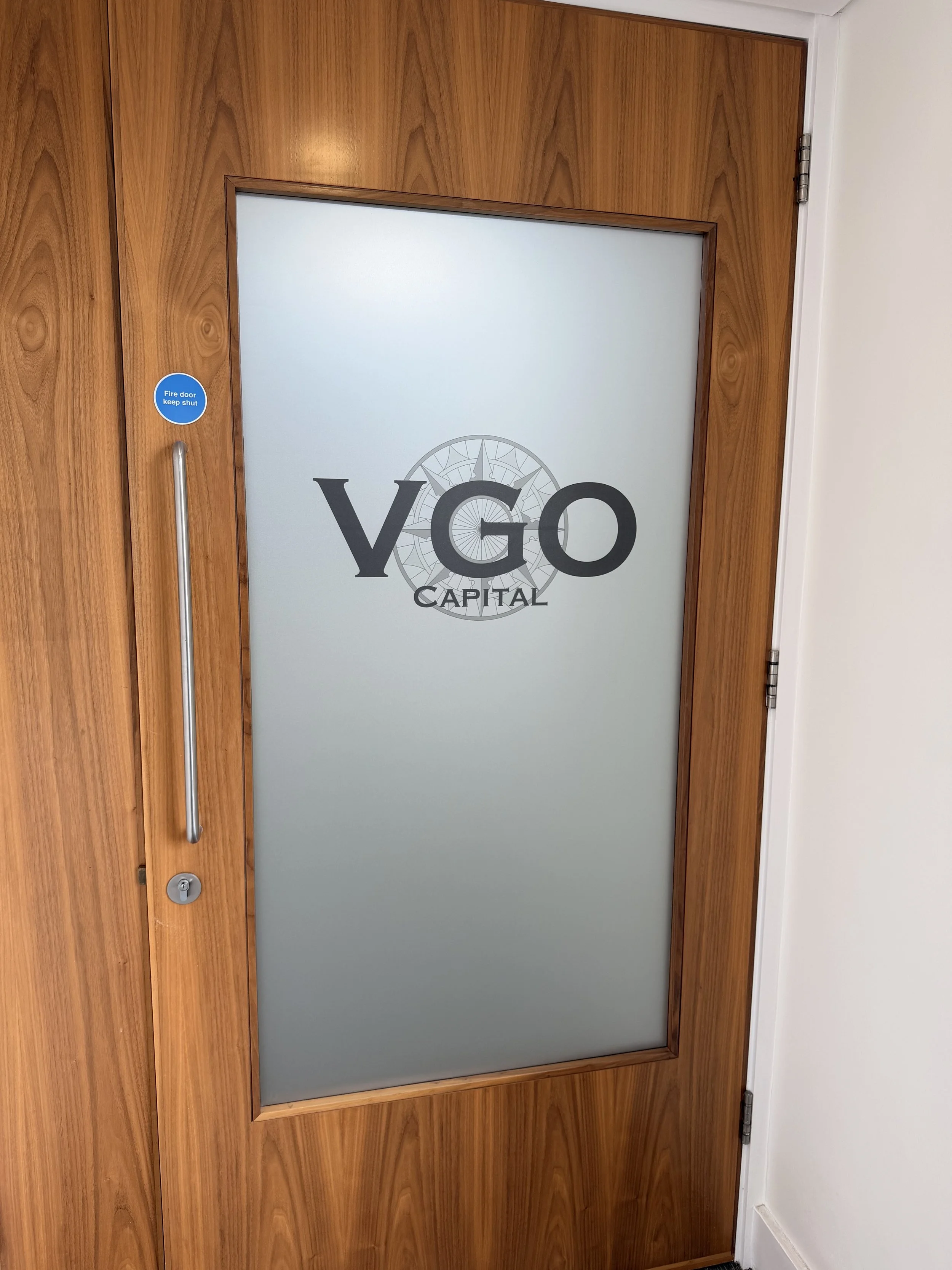 Wooden door with a frosted glass panel displaying the logos for YGO Capital and a compass design.