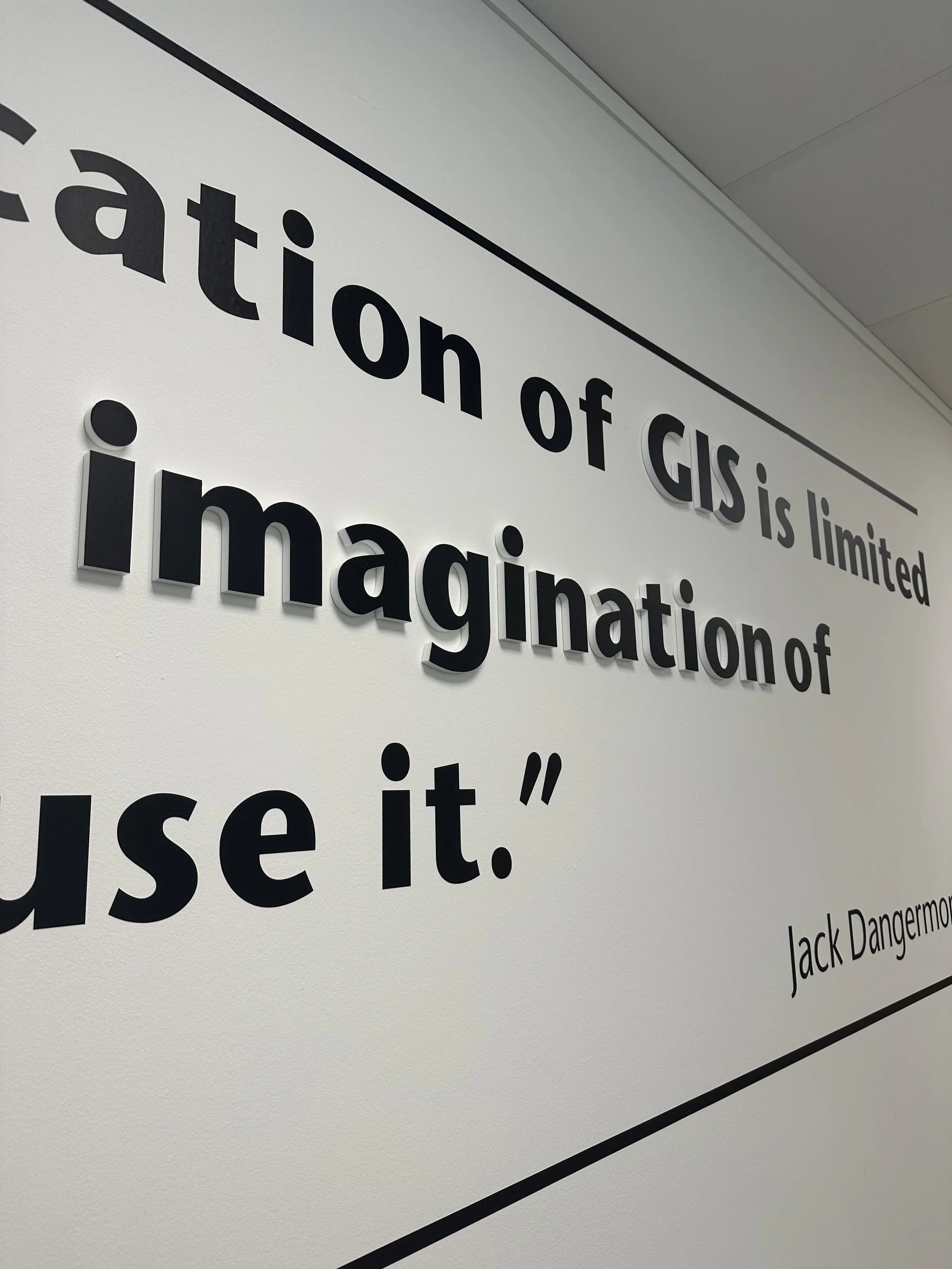Close-up view of an acrylic wall logo with a quote that reads 'The creation of GIS is limited only by imagination,' attributed to Jack Dangers.